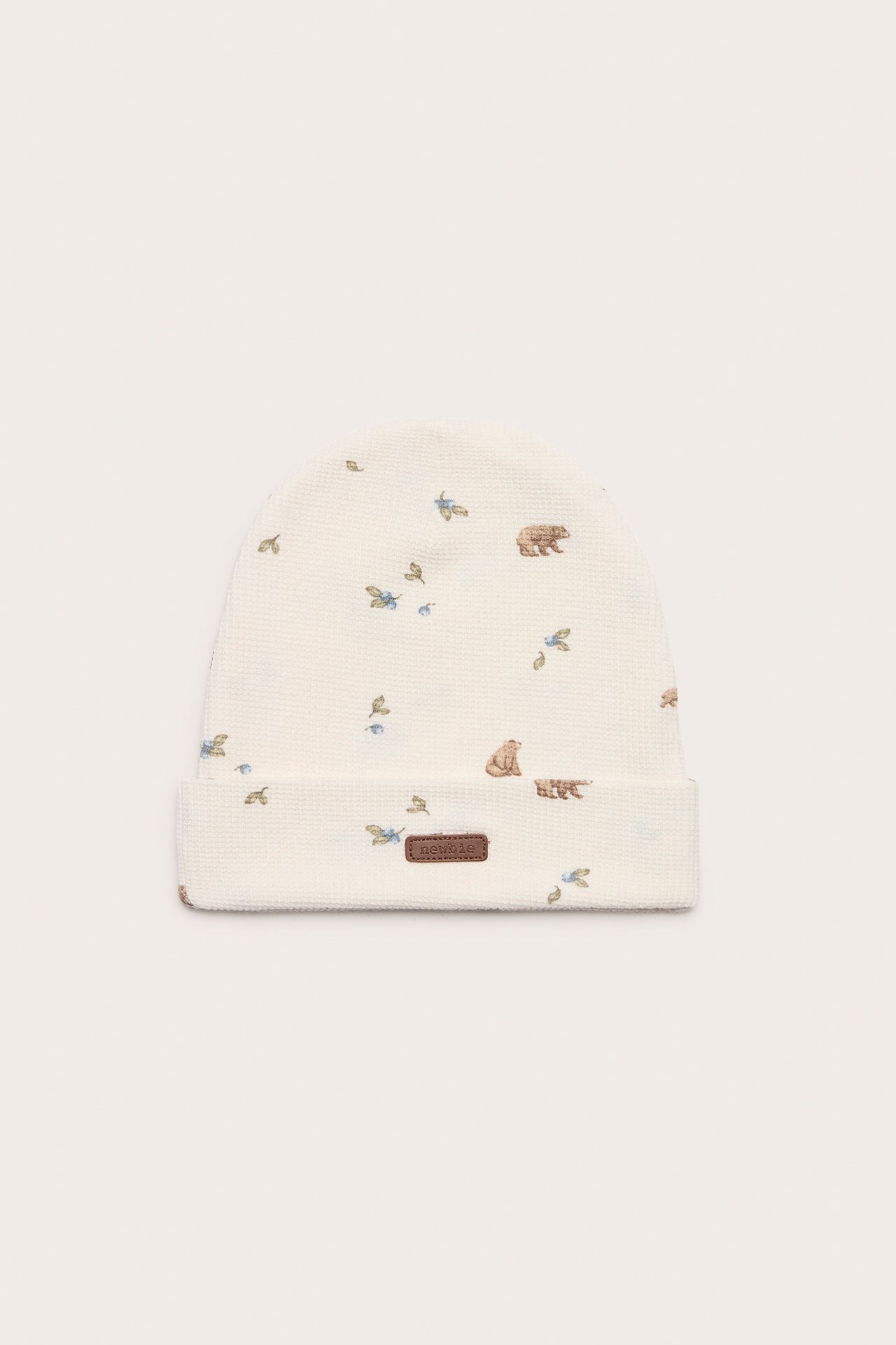 Front view: Off-white baby beanie with waffle knit, forest animal pattern, folded brim, and brown label.