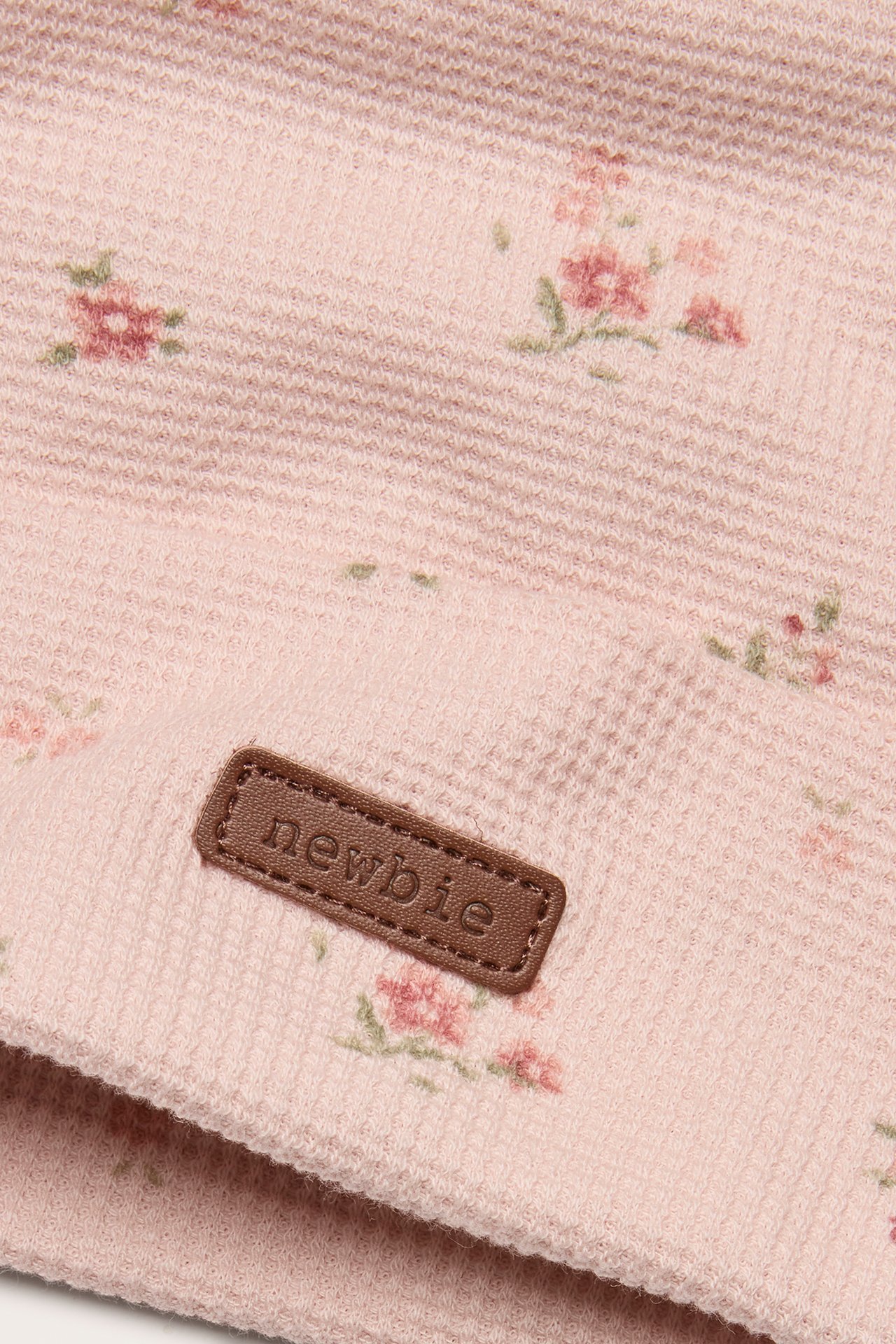 Close-up of a light pink floral patterned jersey beanie with a fold-up brim and brown 'newbie' label.
