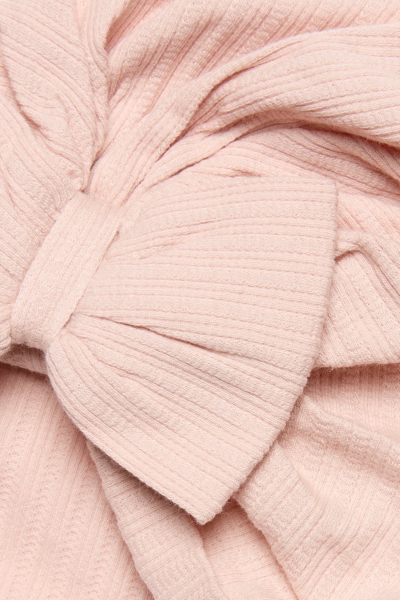 Close-up view of a light pink ribbed jersey baby turban hat with a large bow at the front.