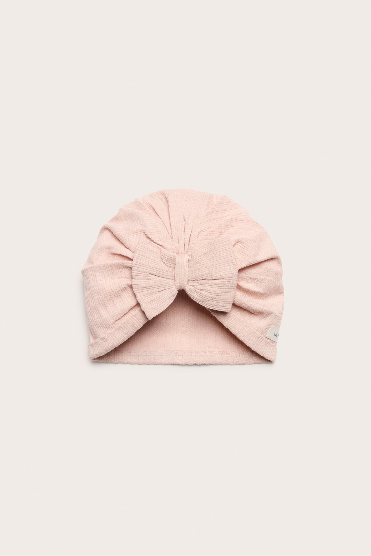 Front view of a light pink ribbed jersey baby turban hat with a large bow at the front.
