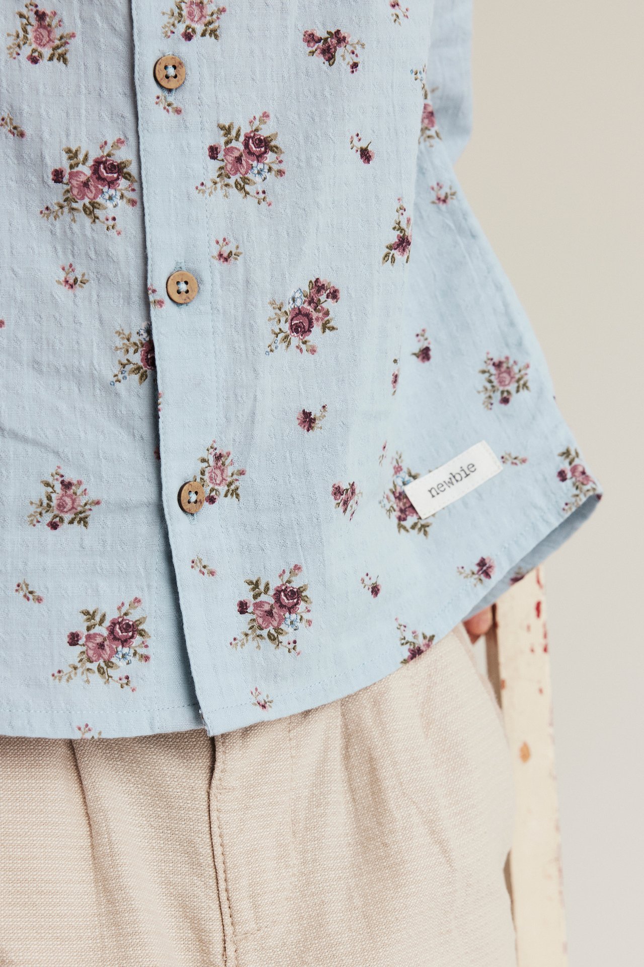 Close-up of a kid wearing a light blue floral woven shirt with wooden buttons over beige pants.