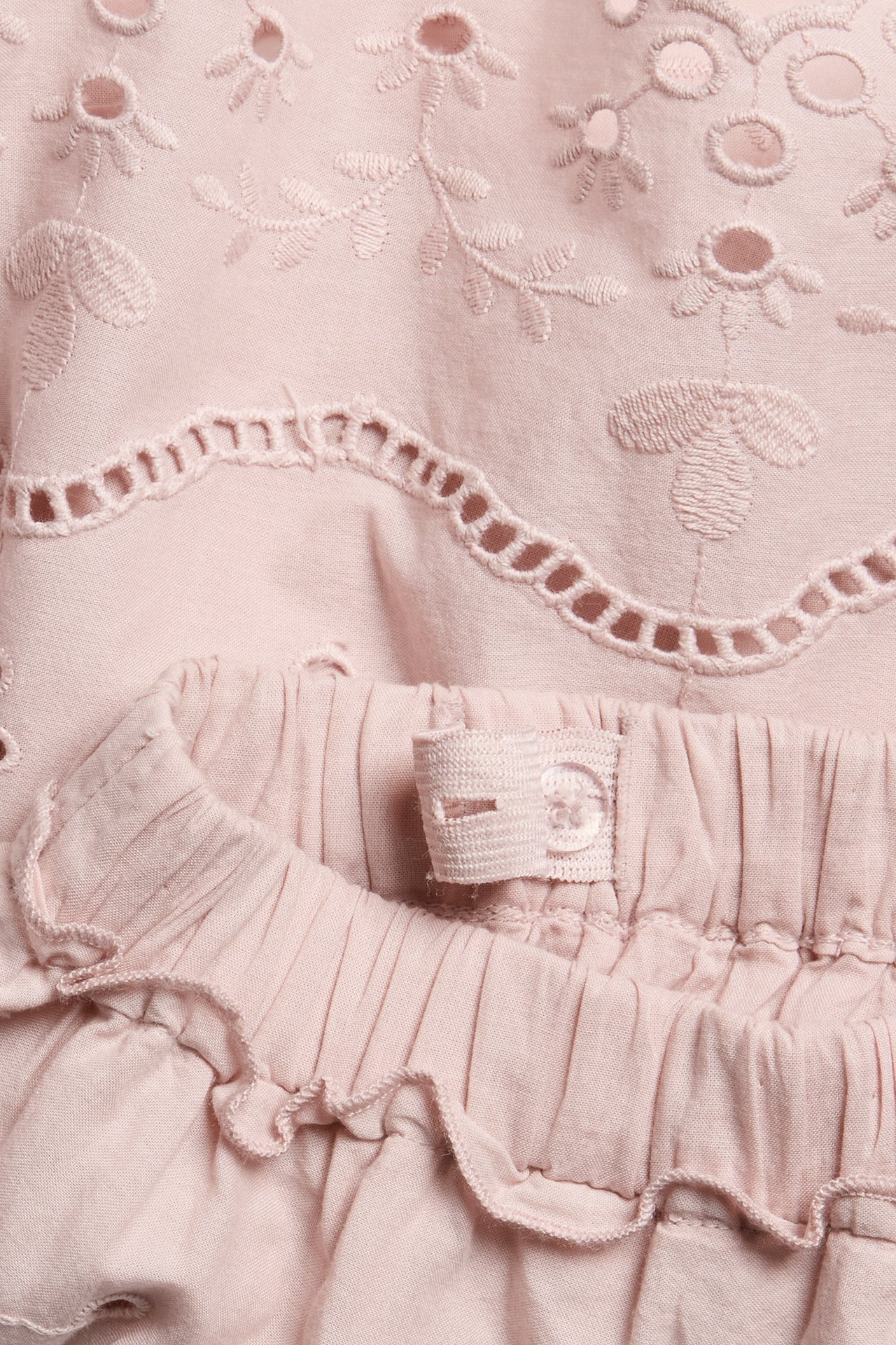 Close-up view of a pink embroidered skirt with floral cut-outs, an adjustable elastic waist, and a mini ruffle.