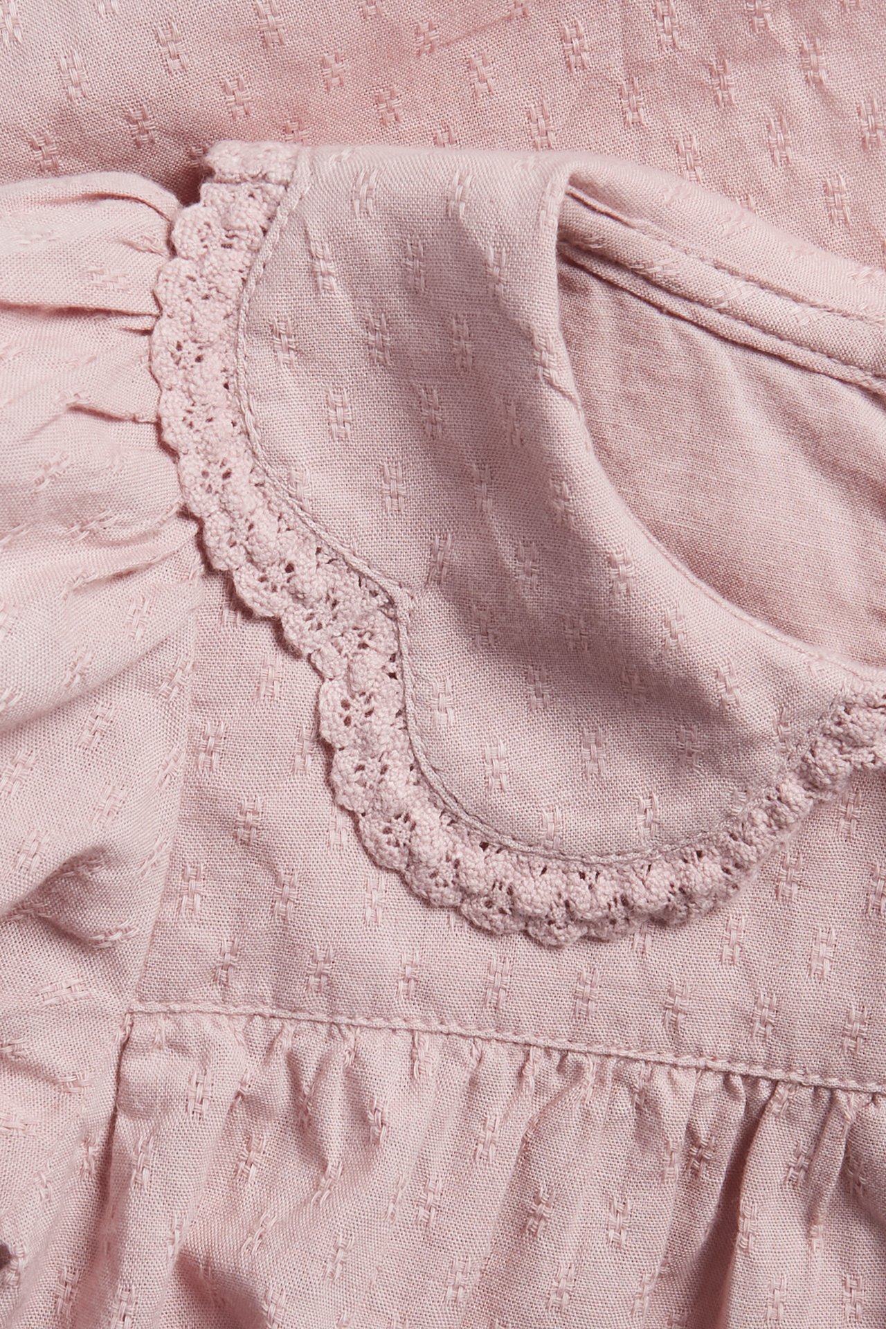 Close-up of a pink baby body with textured woven fabric, a scalloped lace-edged collar, and puff sleeves.