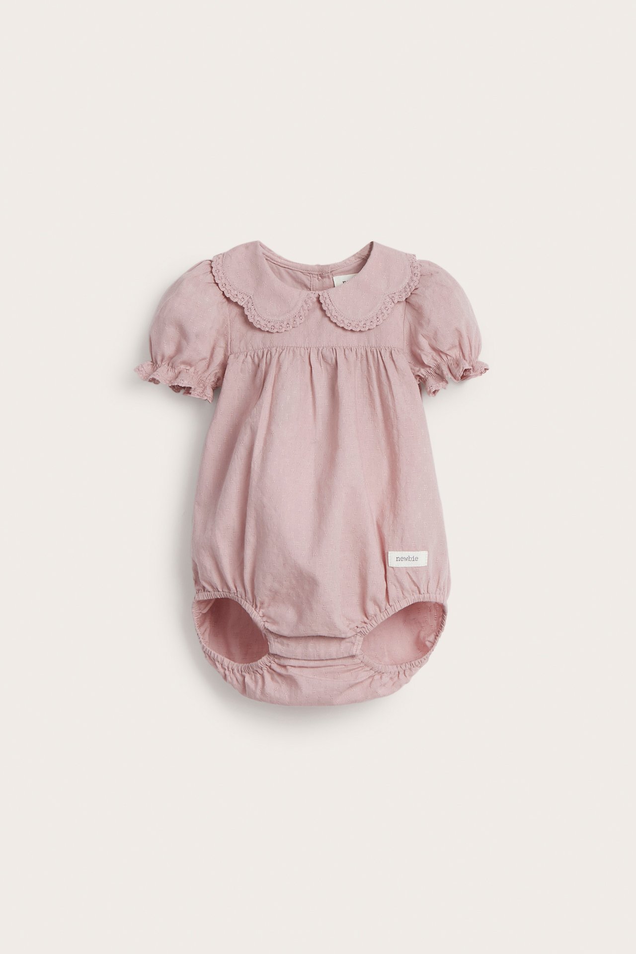 Front view: Pink woven cotton baby bodysuit with lace collar, puff sleeves, elastic legs, and back buttons.