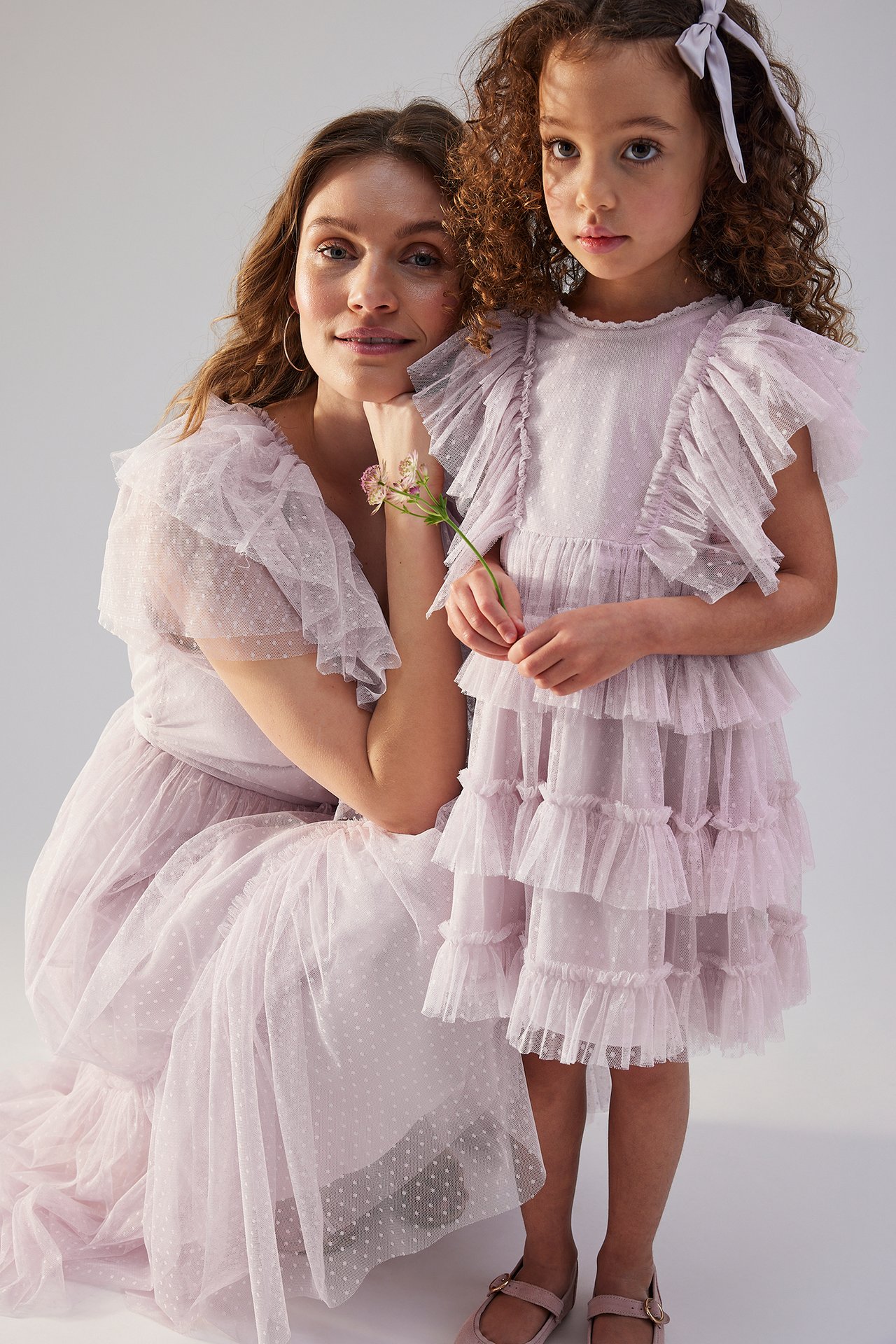 Front view: Kid and woman in matching light lilac dotted mesh dresses with ruffles.
