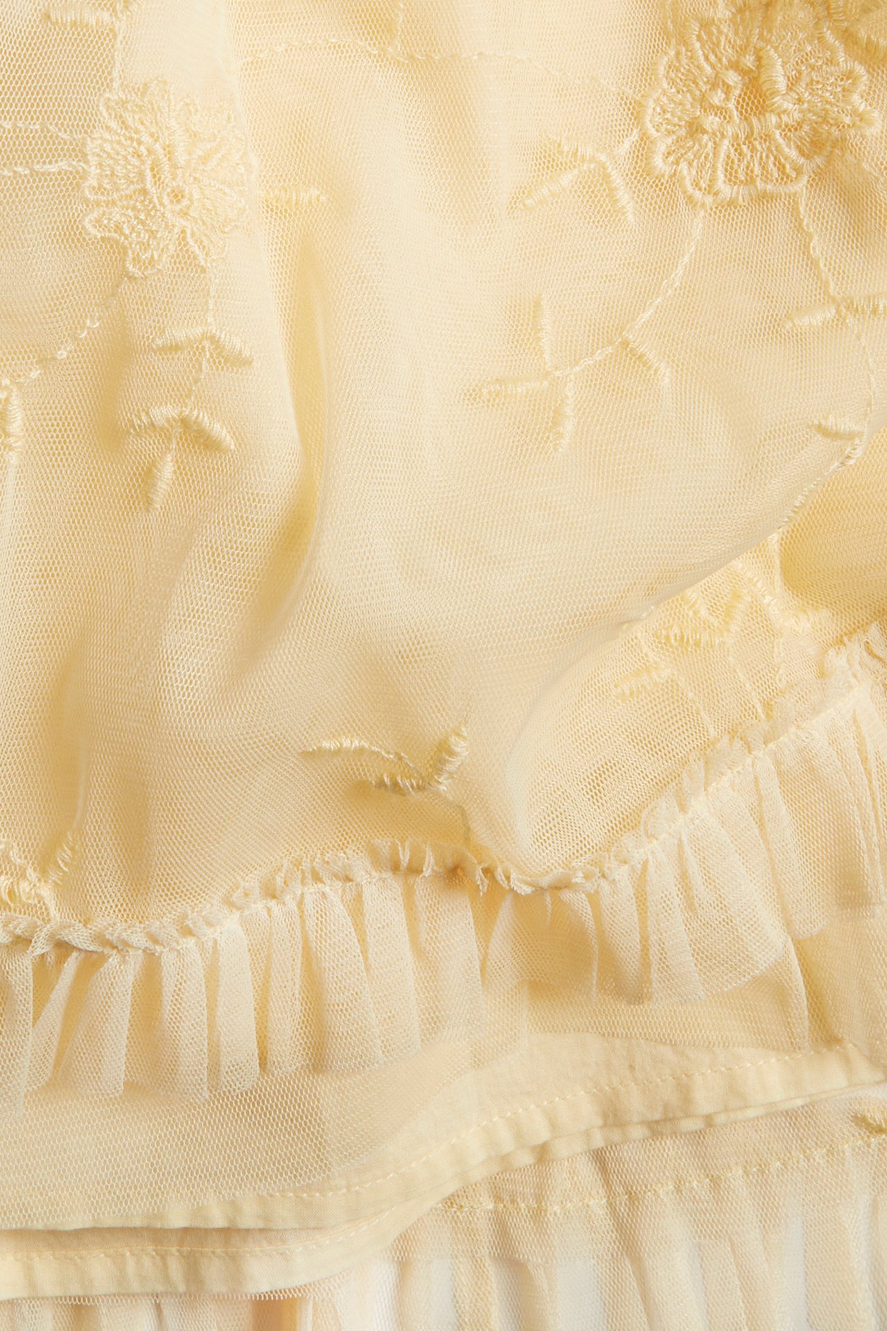 Close-up of a light yellow sheer dress fabric with floral embroidery and a gathered frill.