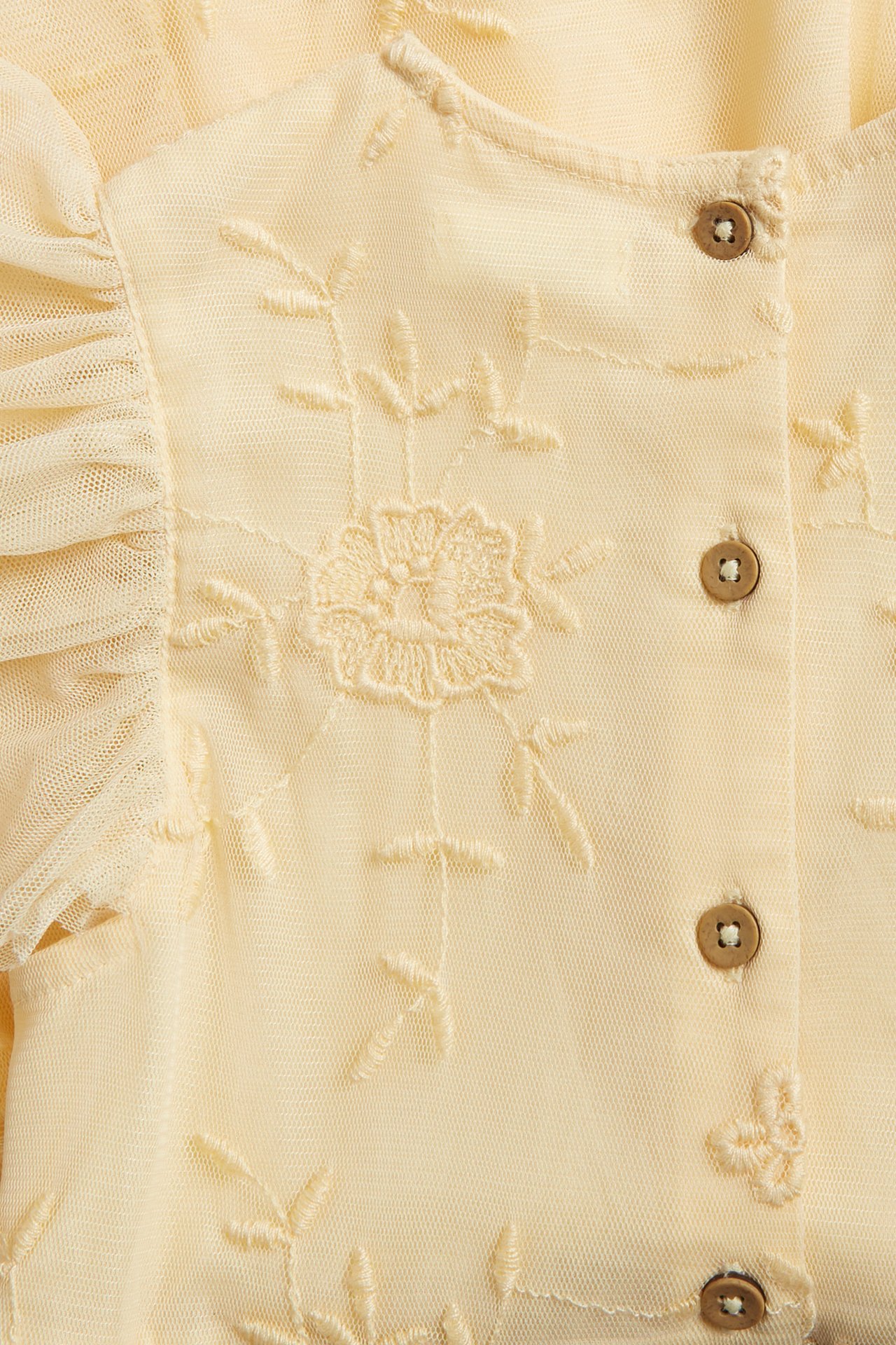 Close-up front view of a yellow dress with floral embroidery, ruffled sleeves, and brown buttons.