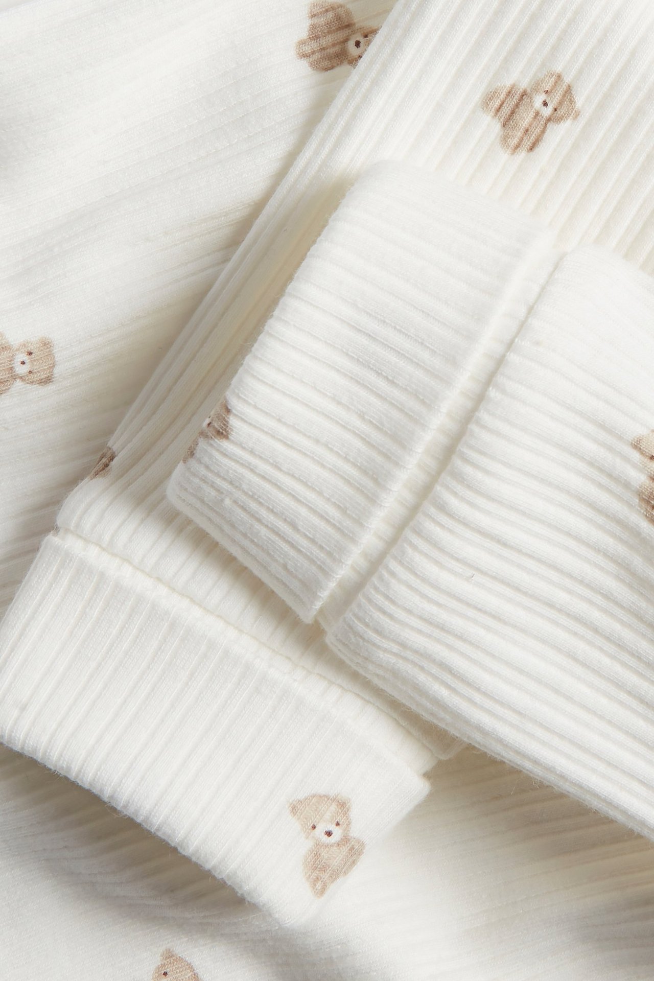 Close-up of offwhite ribbed cotton leggings with a brown teddy bear pattern and foldable cuffs.