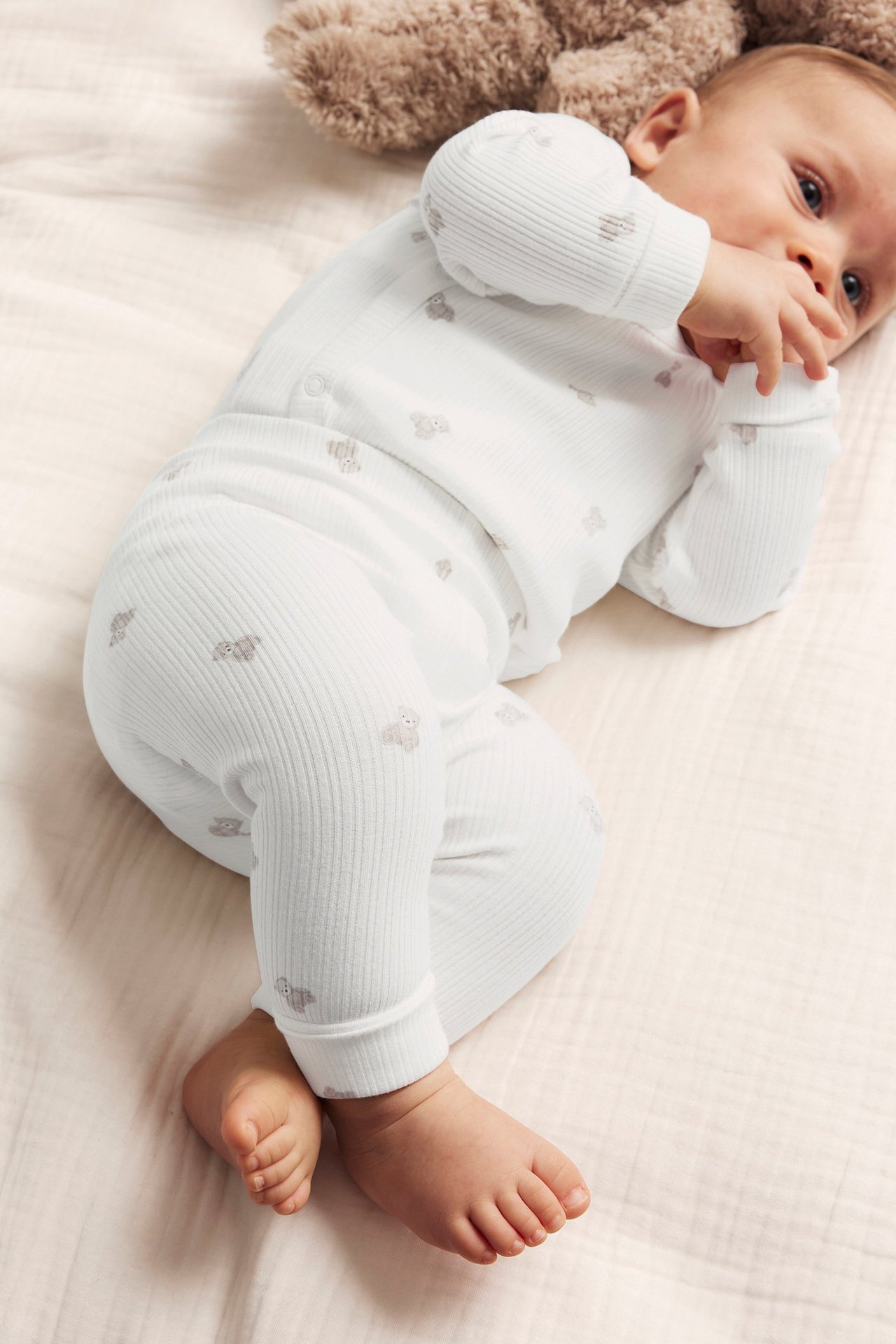 Top-down view of a baby in off-white ribbed leggings and matching long-sleeve top with teddy bear pattern.
