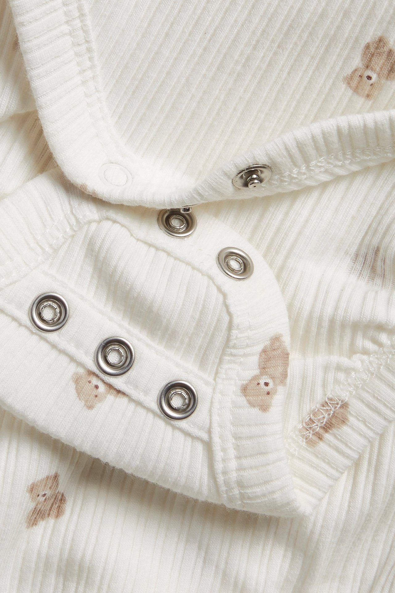 Nahaufnahme eines cremeweißen gerippten Baby-Wickelbodys mit Teddybärmuster und Druckknöpfen.