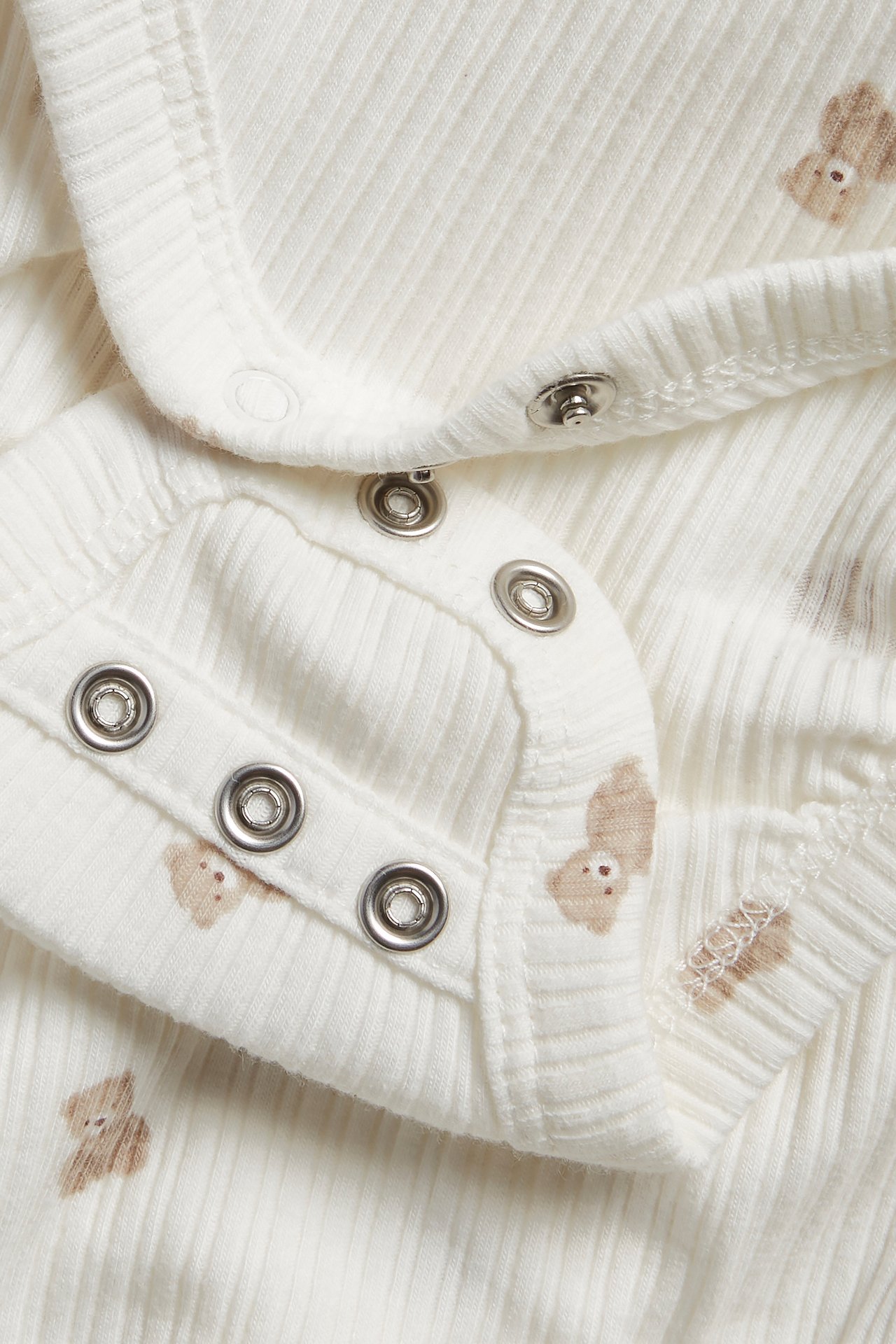 Close-up of an off-white ribbed baby wrap-around bodysuit with a teddy bear pattern and snap buttons.