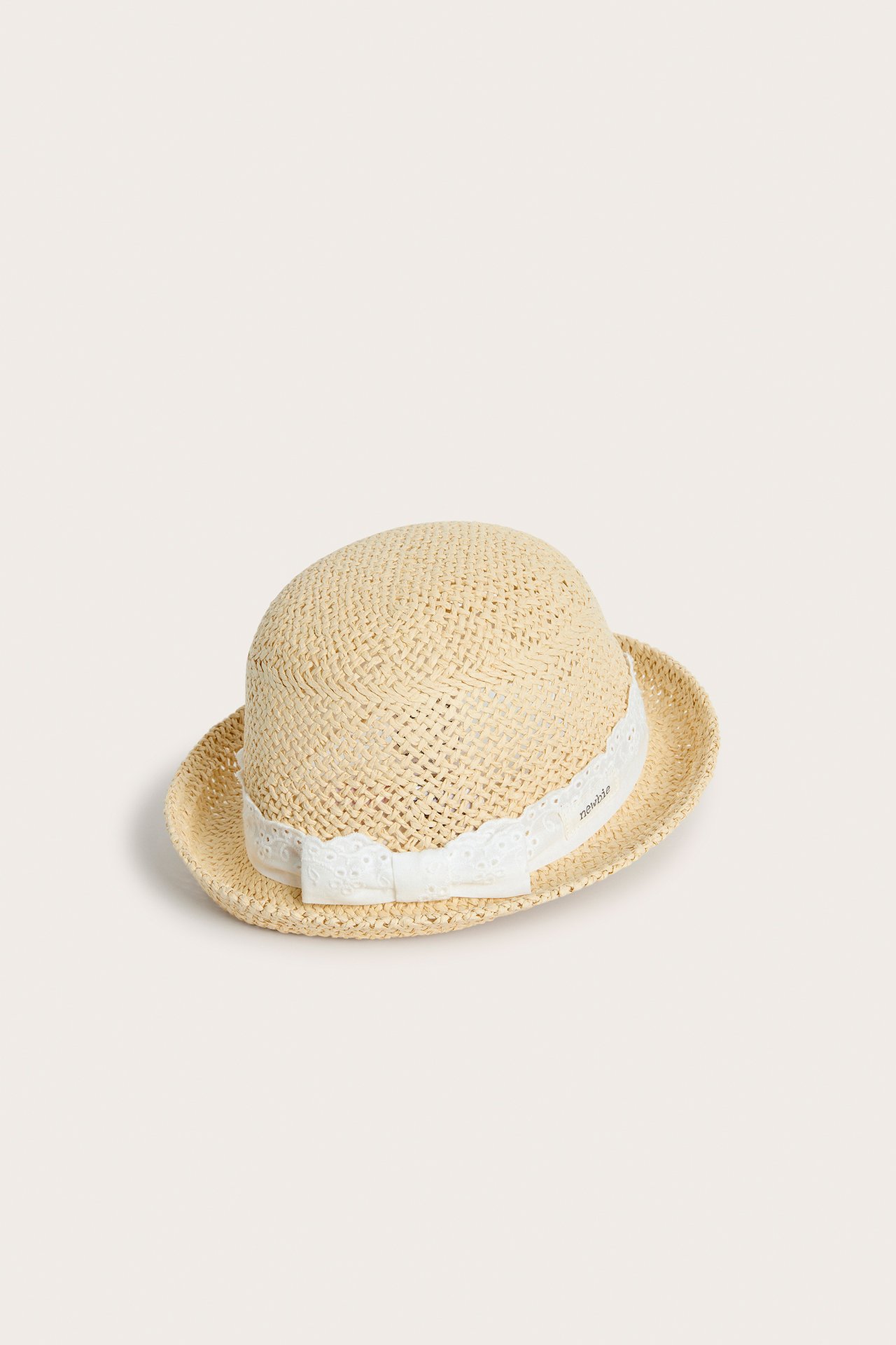 Front-side view of a light beige straw hat for baby/kid with a white lace band and bow.