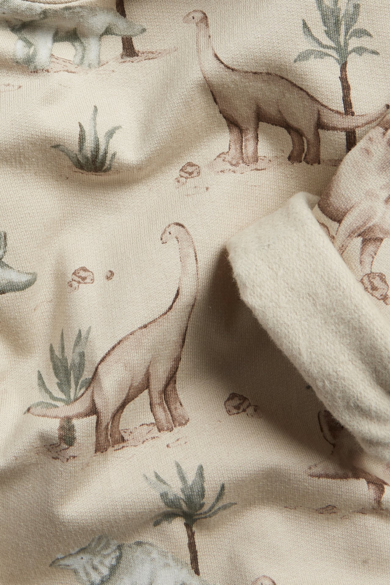 Close-up of a beige cotton hoodie fabric with a brown dinosaur pattern and a visible brushed inside.