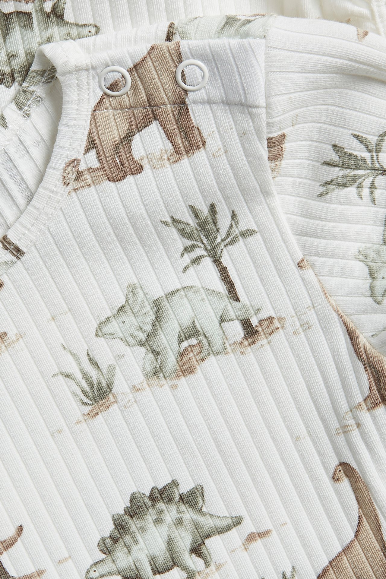 Close-up of an off-white ribbed baby bodysuit with a dinosaur and palm tree pattern, featuring snap buttons.