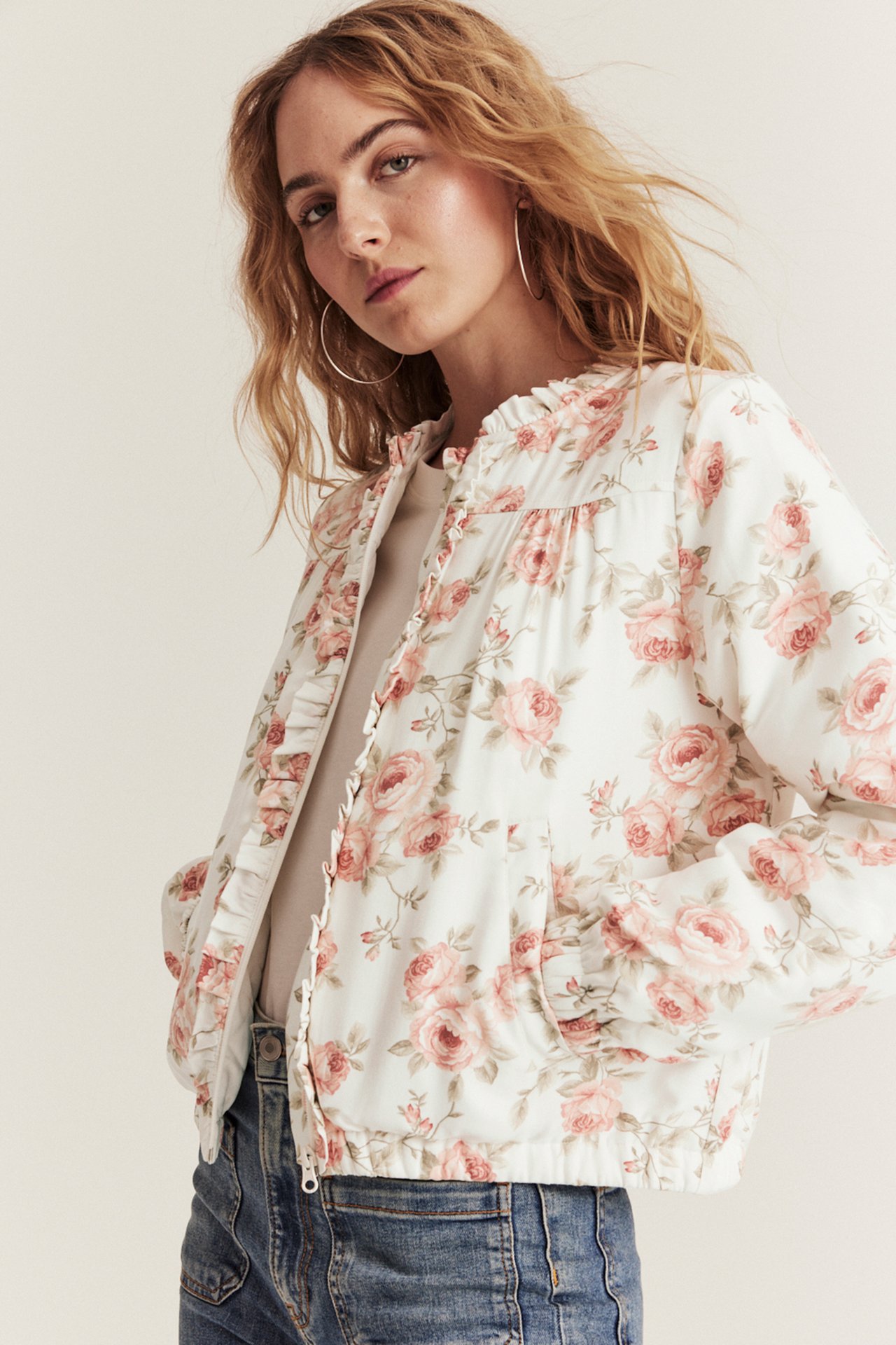 Printed offwhite bomber jacket with small ruffle collar, two front pockets, worn by woman.