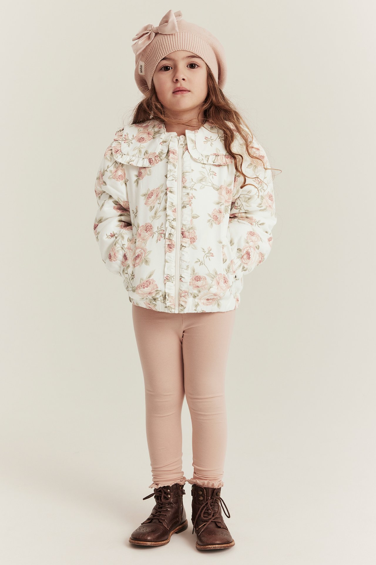 Front view: Kid in off-white floral bomber jacket with ruffles, pink leggings, pink beret, brown boots.