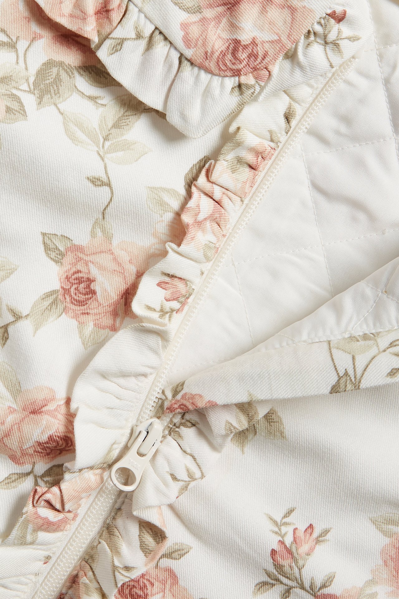 Close-up of an off-white floral bomber jacket with pink roses, ruffled collar, and zipper with ruffles.