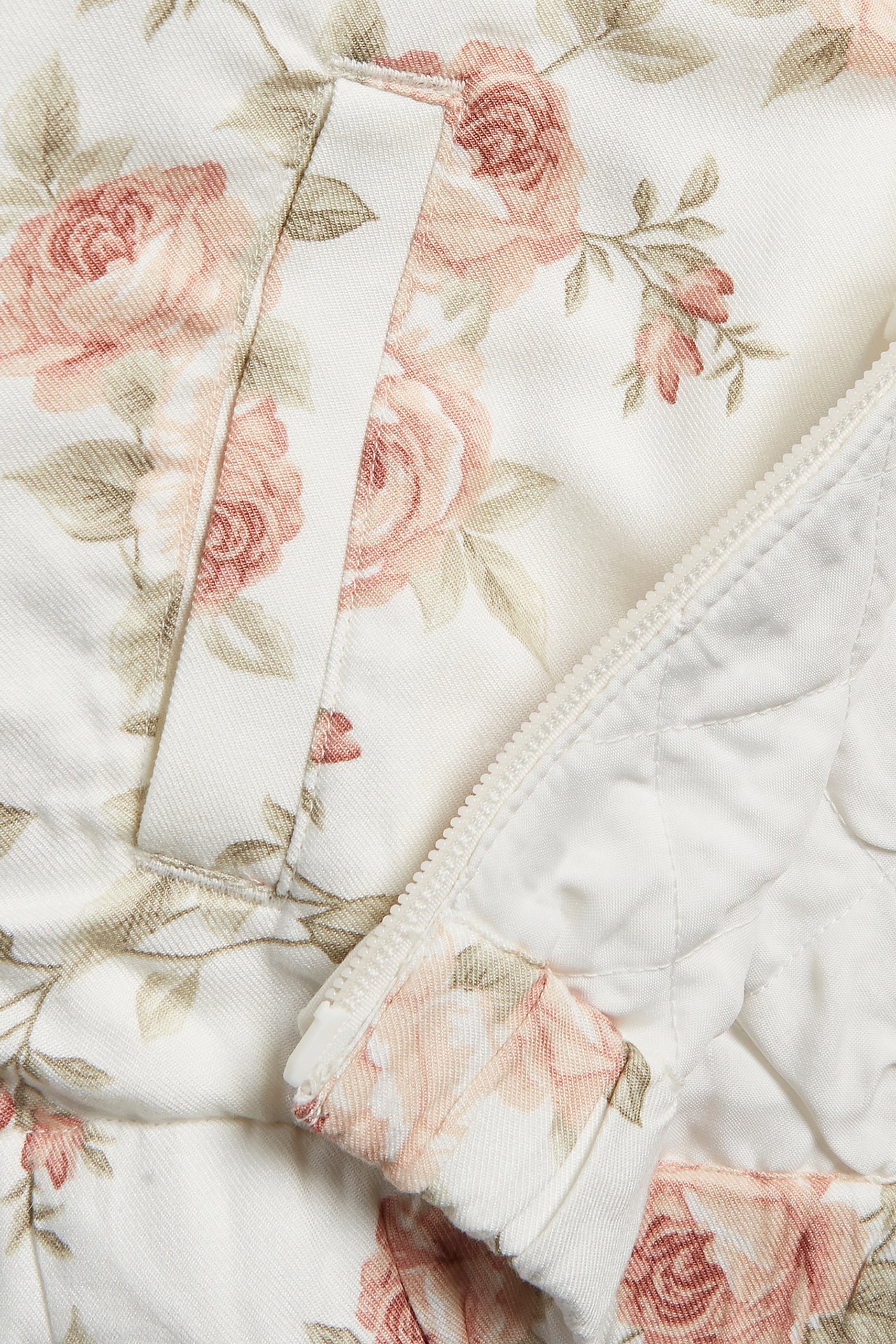 Close-up of an off-white floral bomber jacket with pink roses, a pocket, and a zipper with a ruffle.
