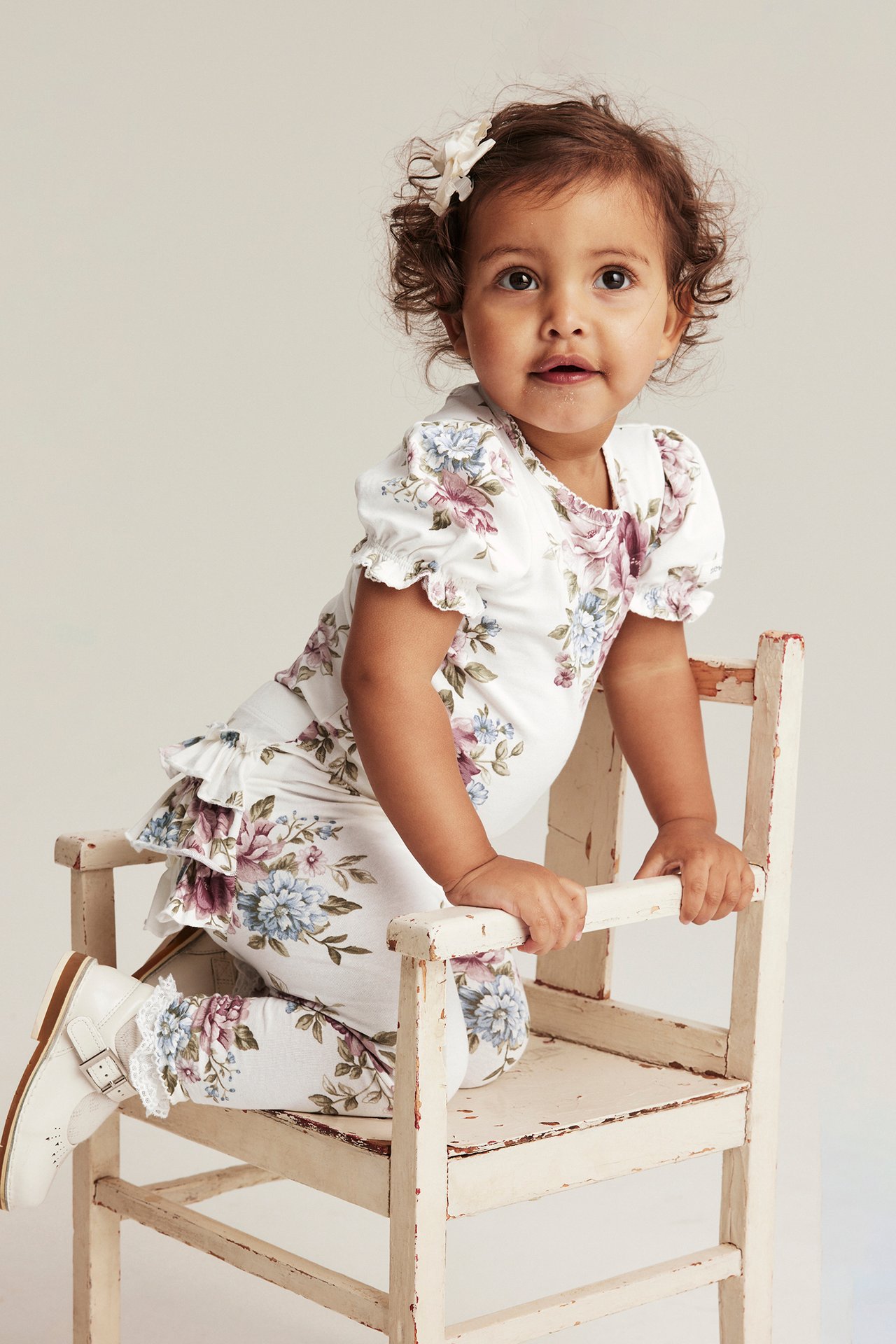 Front view: baby in off-white floral puff-sleeve bodysuit, matching leggings, white shoes, and a hair clip.