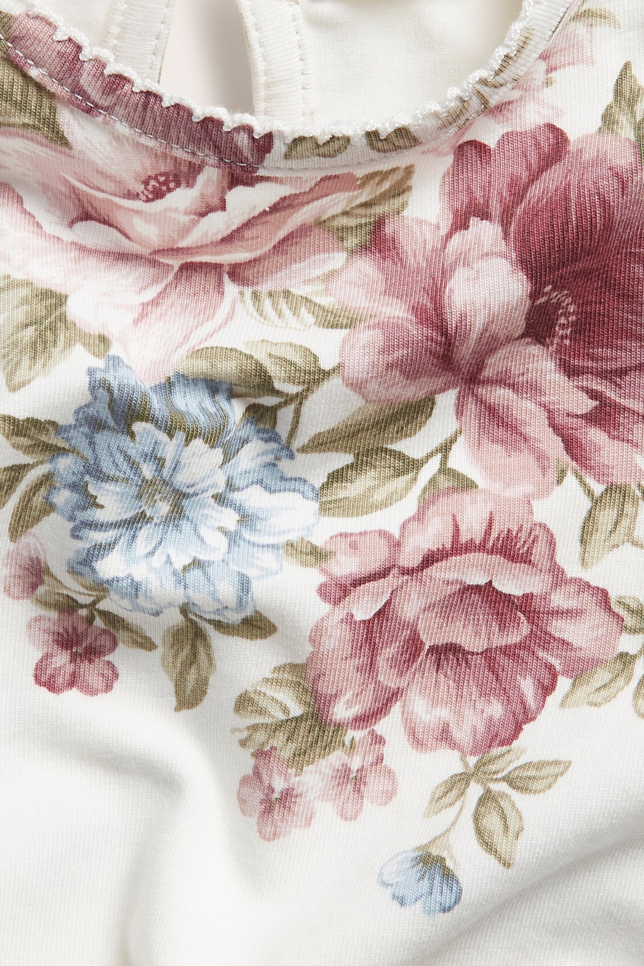 Close-up of an off-white baby bodysuit with a pink and blue floral pattern and picot trim.