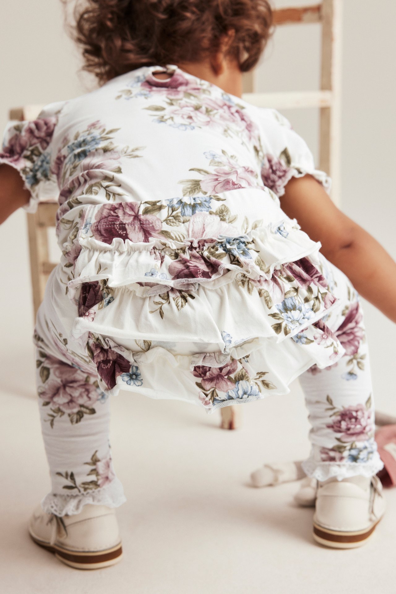 Back view of a baby wearing off-white floral print leggings with ruffles and a matching top.