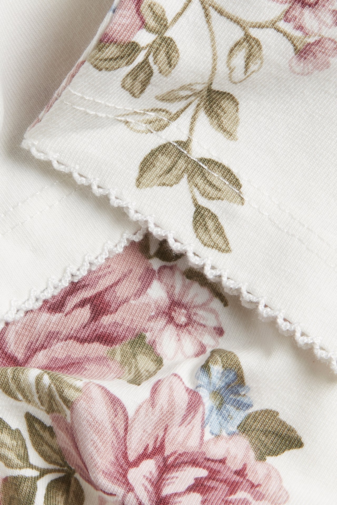 Close-up of off-white cotton jersey leggings with a pink and blue floral pattern and a picot edge.