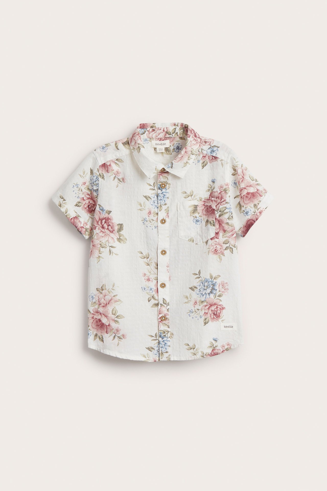 Front view: Kid's off-white short-sleeved organic cotton shirt with pink and blue floral pattern and pocket.