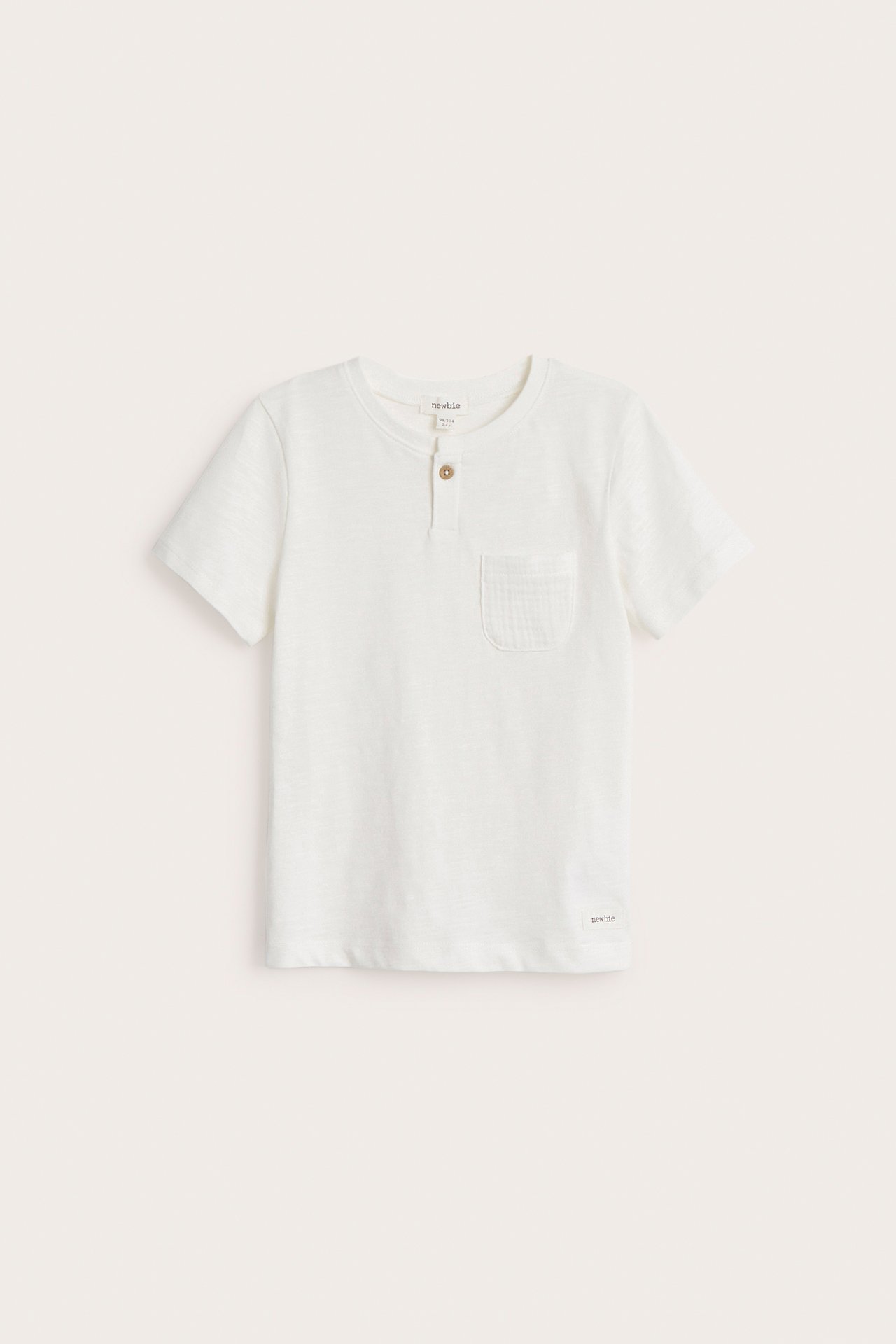 Vorderansicht: Off-weißes Kinder-Slub-Jersey-T-Shirt mit kurzen Ärmeln, einem Knopf und Brusttasche.