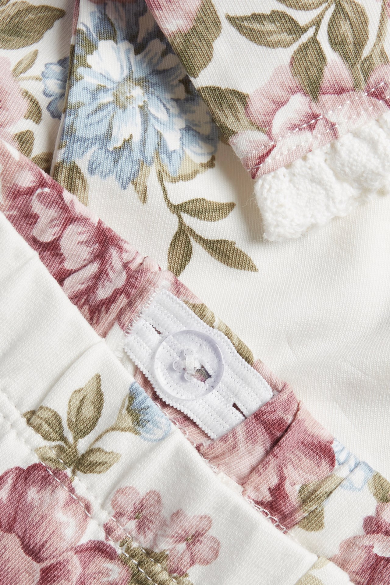 Close-up of off-white floral cotton jersey leggings with adjustable elastic waist and white lace trim.