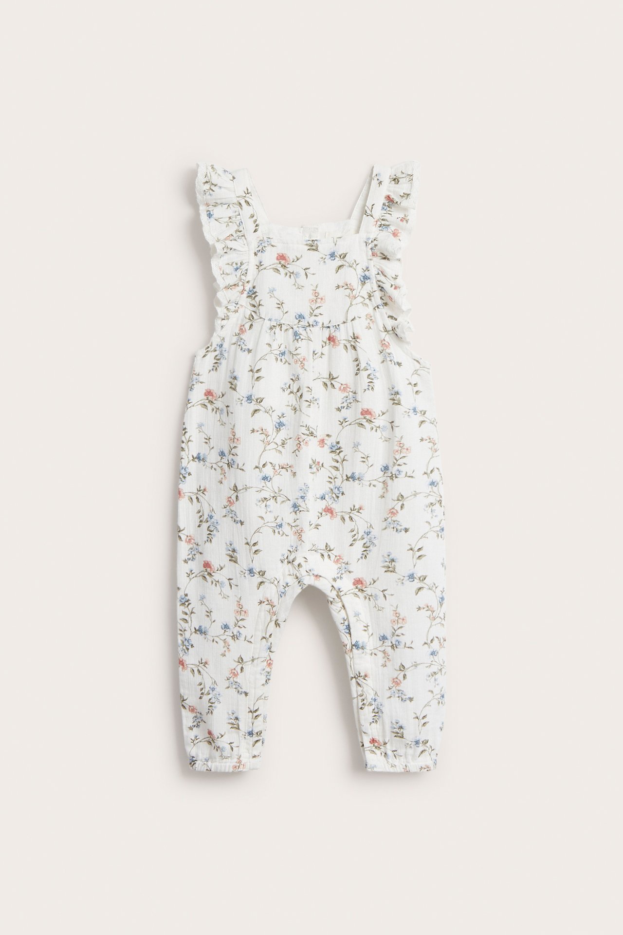 Vorderansicht eines cremefarbenen Baby-Blumen-Baumwollstramplers mit Rüschenträgern, Druckknöpfen und elastischen Beinabschlüssen.