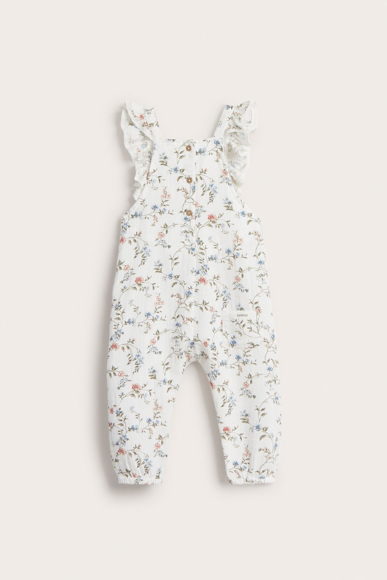 Vorderansicht eines cremeweißen Baby-Blumen-Baumwoll-Overalls mit Rüschenträgern, Druckknöpfen und elastischen Knöcheln.