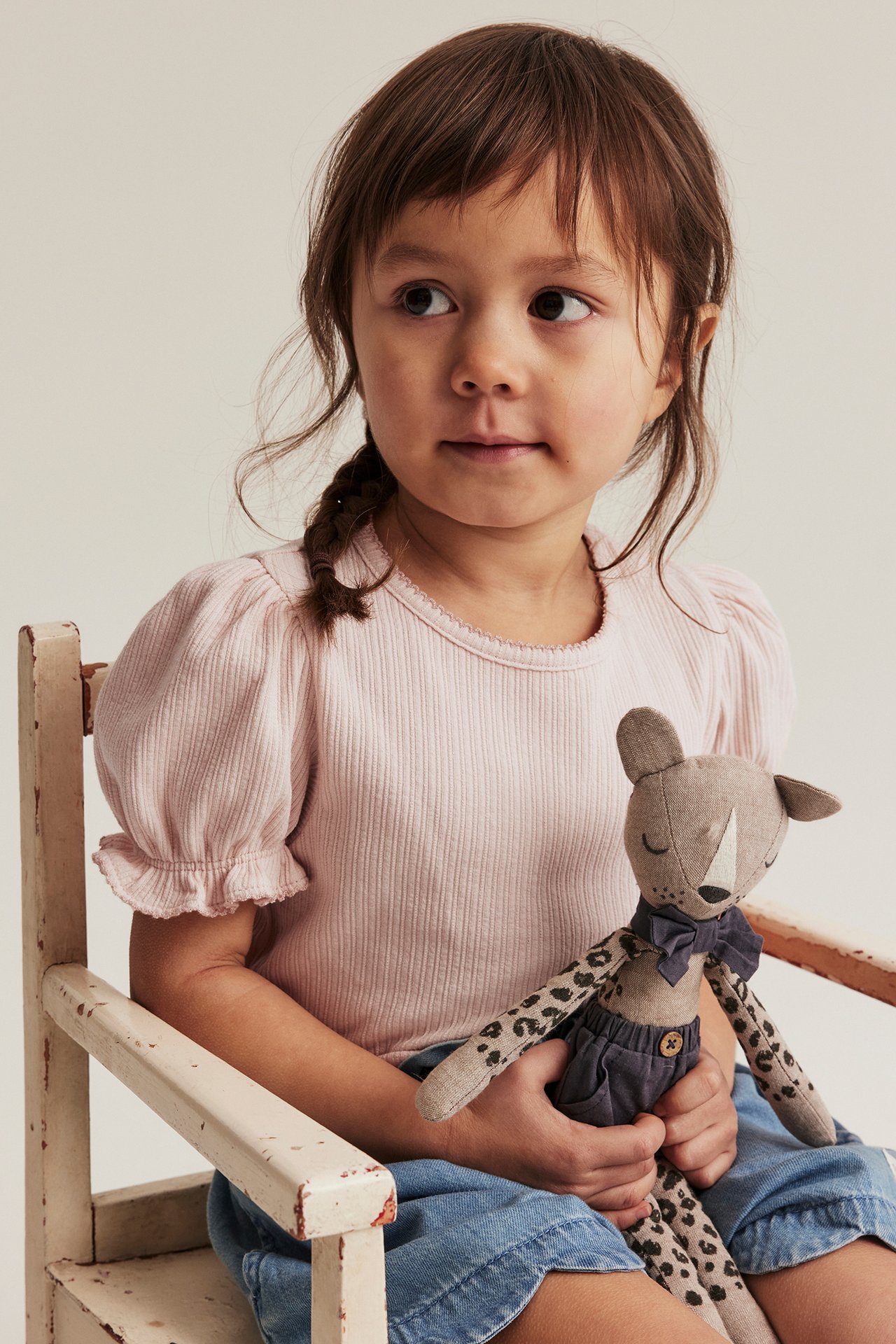 Front view: Kid in light pink ribbed puff-sleeve top with picot trim, blue shorts, holding a plush toy.