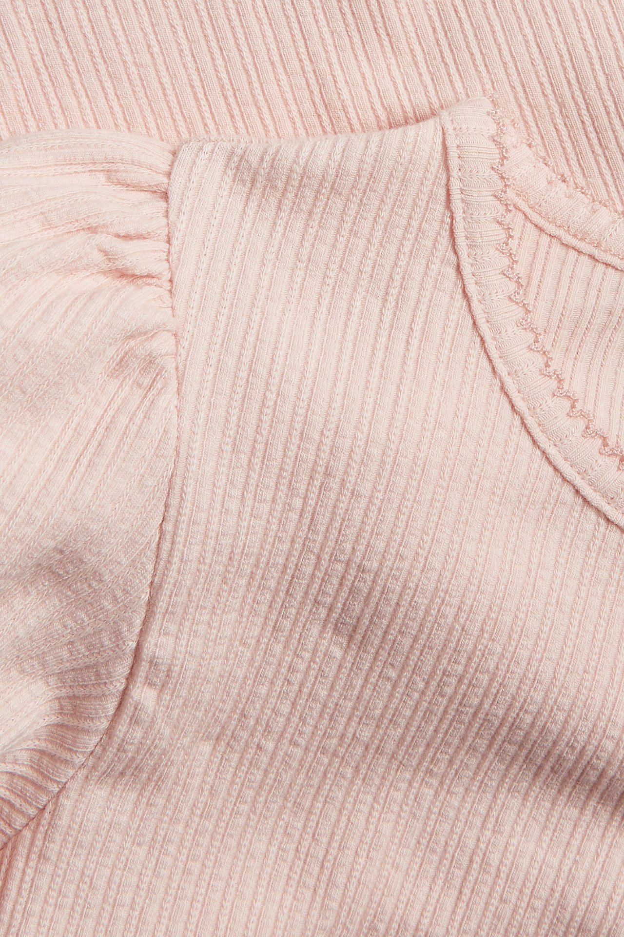 Close-up of a light pink ribbed jersey top with short puff sleeves and picot trim.