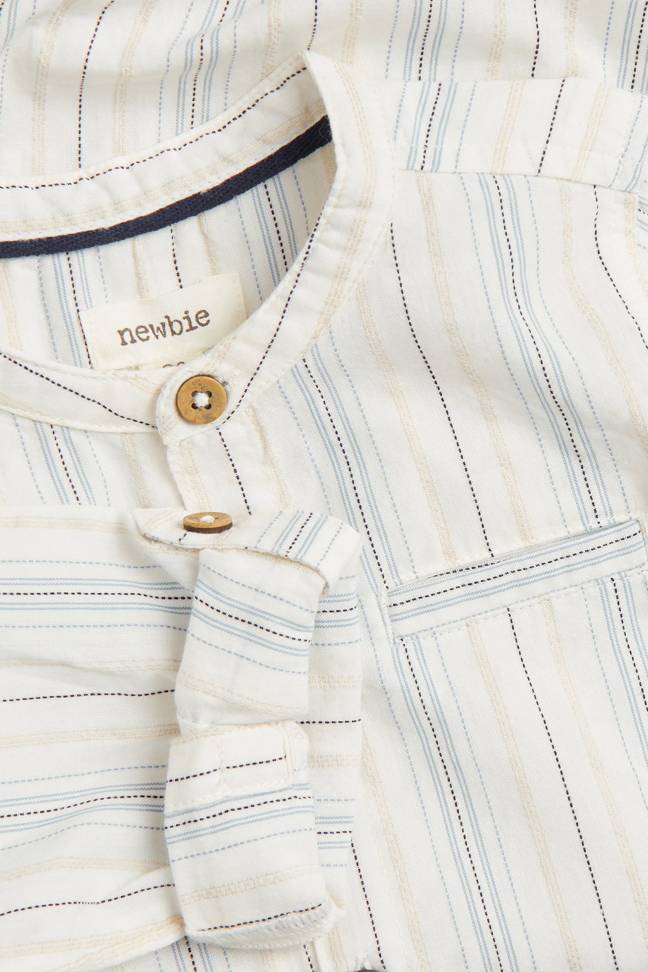 Close-up of a baby's off-white striped organic cotton shirt-bodysuit with mandarin collar, wooden buttons, and rolled sleeves.
