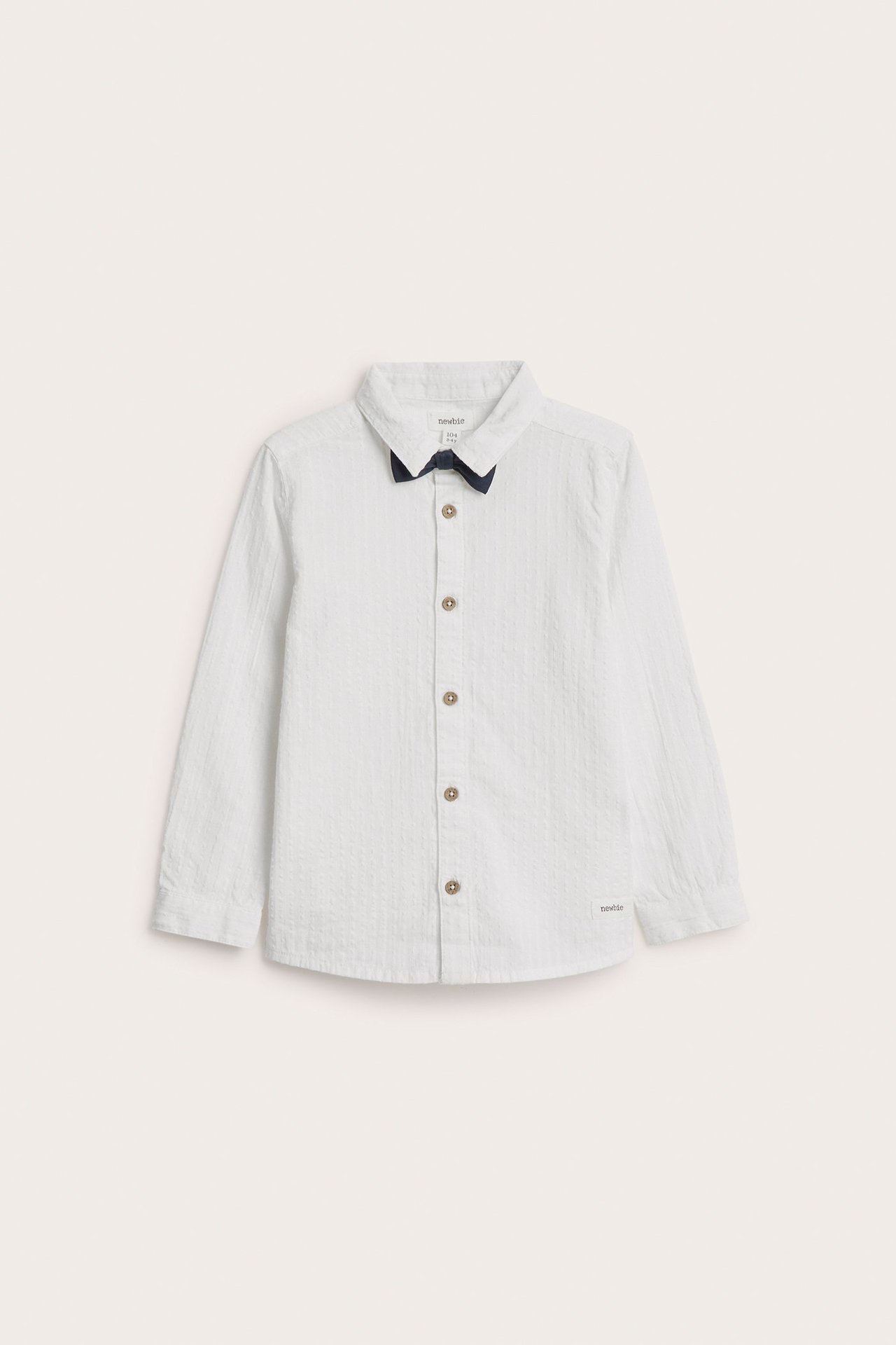 Front view of a kid's off-white woven cotton shirt with brown buttons and a navy detachable bow tie.
