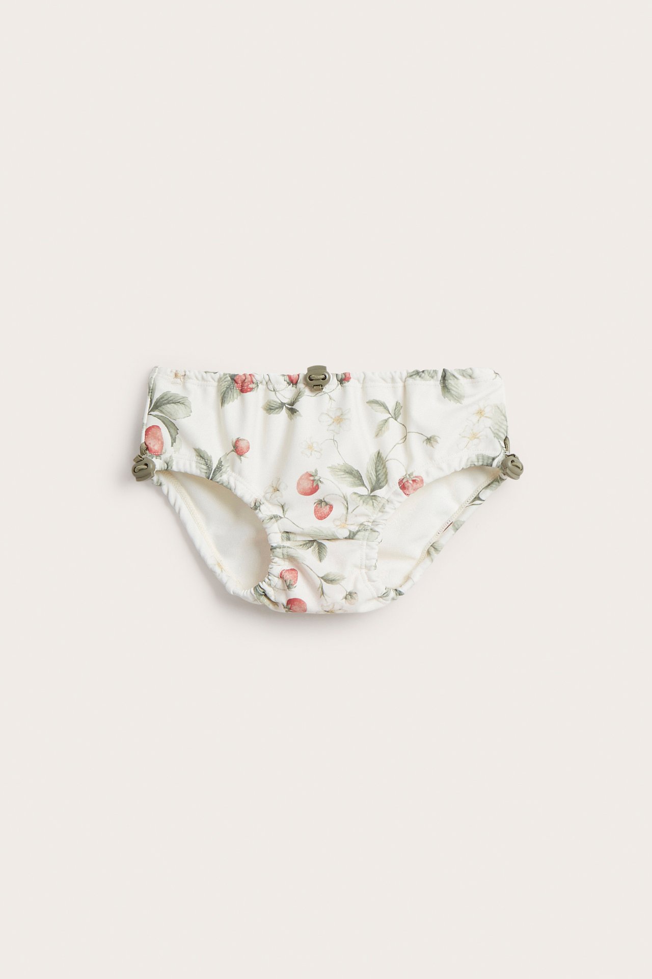 Vorderansicht von cremeweißen Baby-Badehosen mit rotem Erdbeermuster und olivgrünen Kordelstoppern.