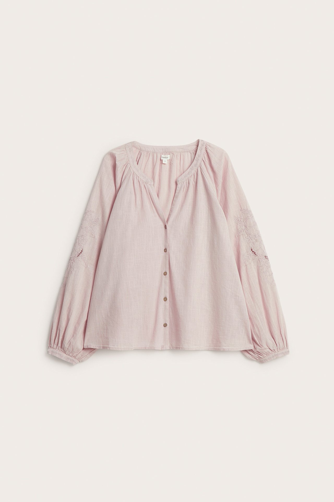 Vorderansicht einer rosa gewebten Baumwollbluse mit Stickereien an den Ärmeln und Knopfleiste vorne.