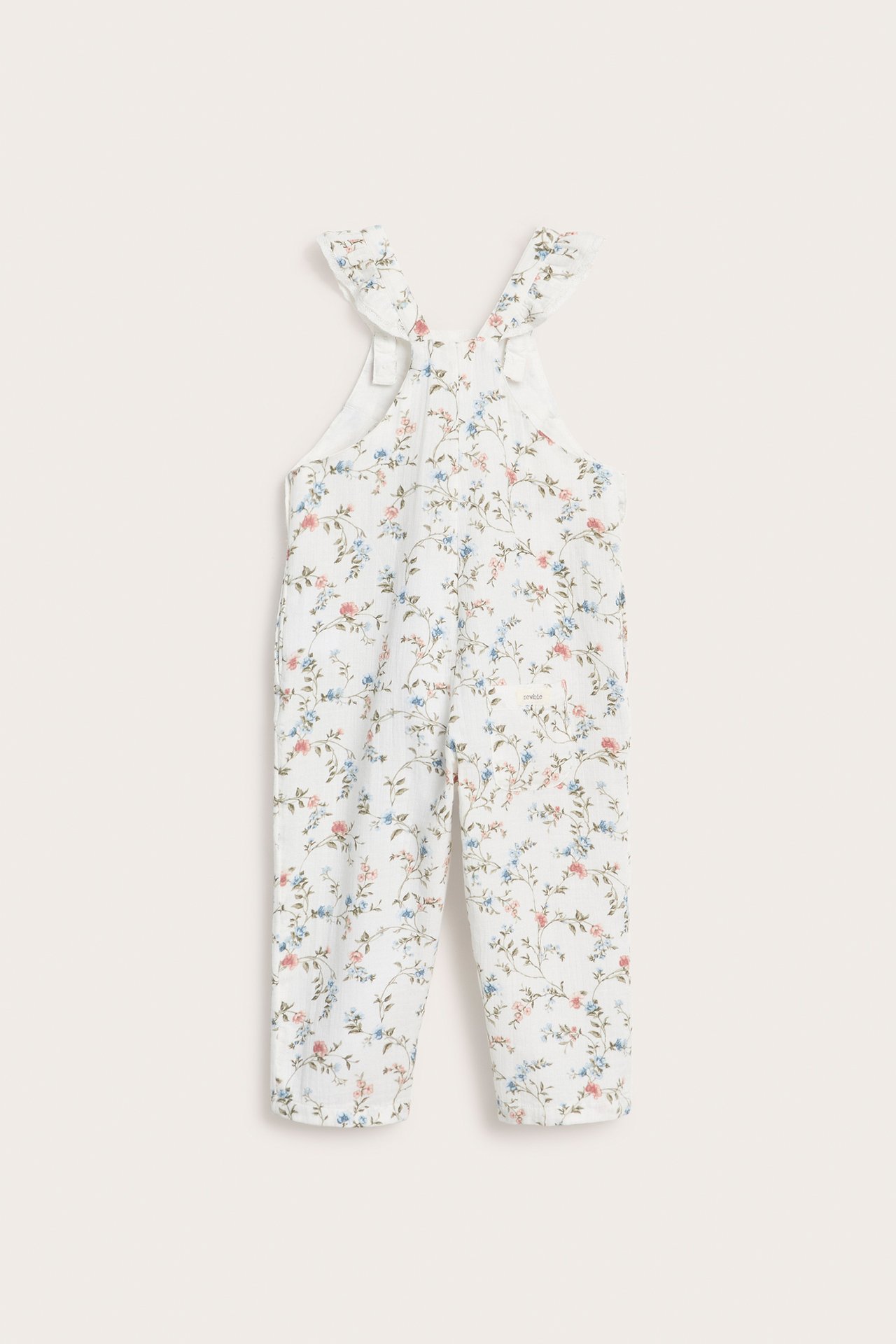 Vorderansicht von Kinder-Latzhose aus cremefarbener Baumwolle mit Blumenmuster, Rüschen-Trägern und seitlichen Knöpfen.