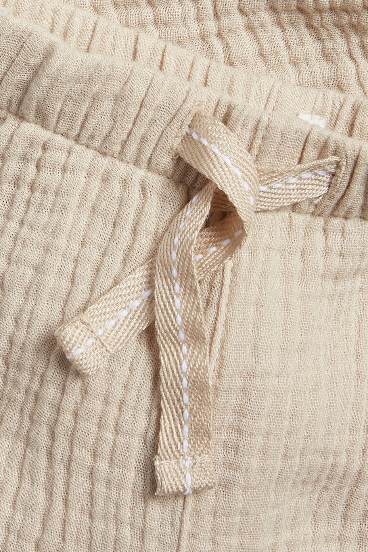 Nahaufnahme beiger Baumwoll-Musselin-Hose mit elastischem Bund und Fischgrät-Kordelzug.
