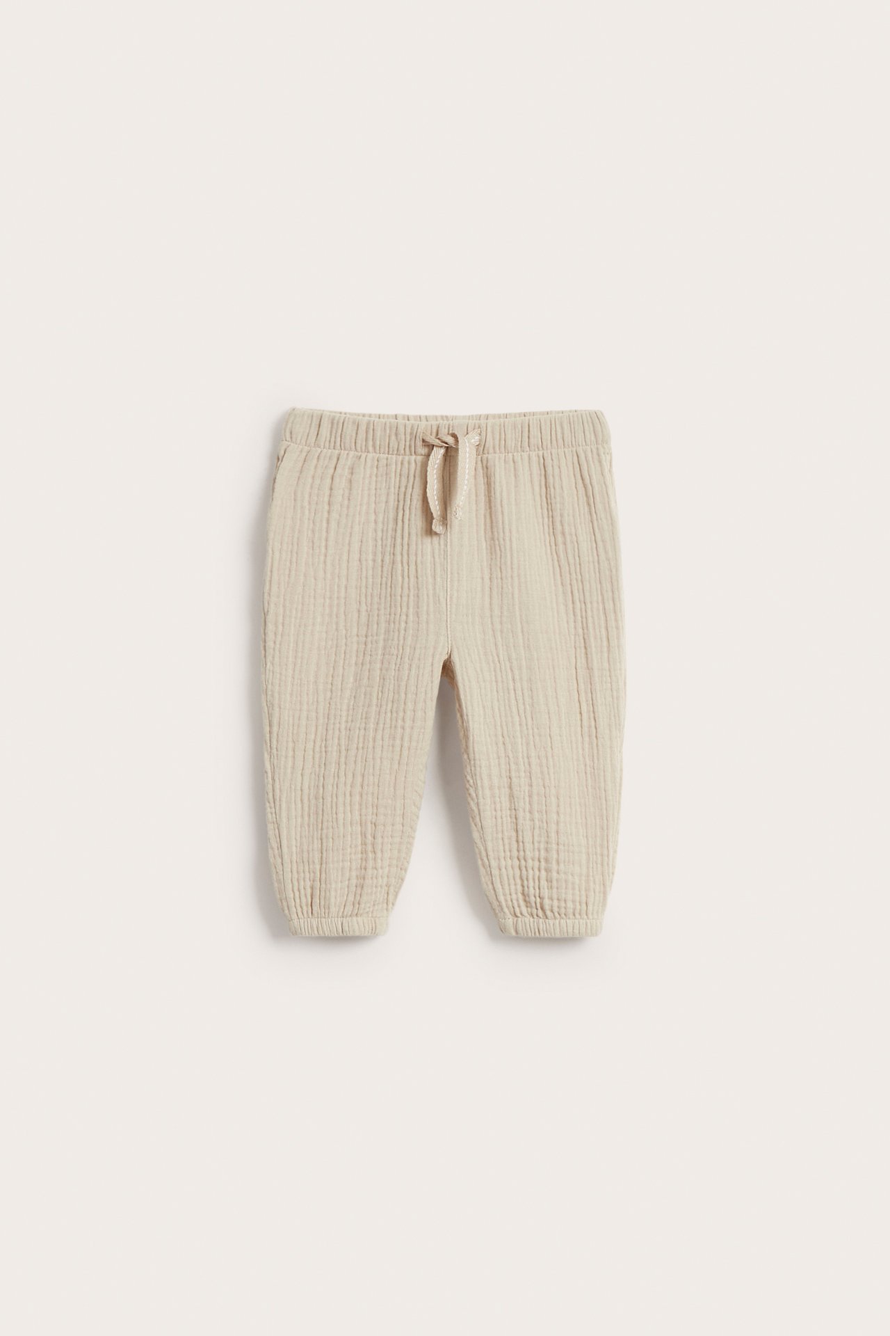Vorderansicht beiger Musselin-Babyhose mit elastischem Bund und Kordelzug.