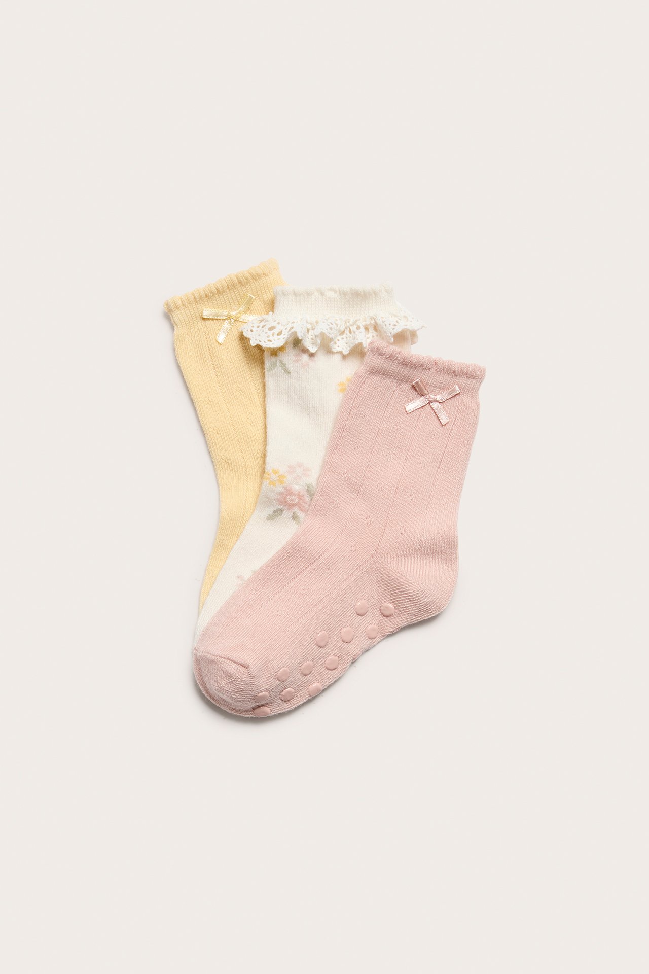 Drei Socken: hellrosa Pointelle mit Antirutsch, cremefarben geblümt mit Spitze, und gelb Pointelle, alle mit Schleifen.
