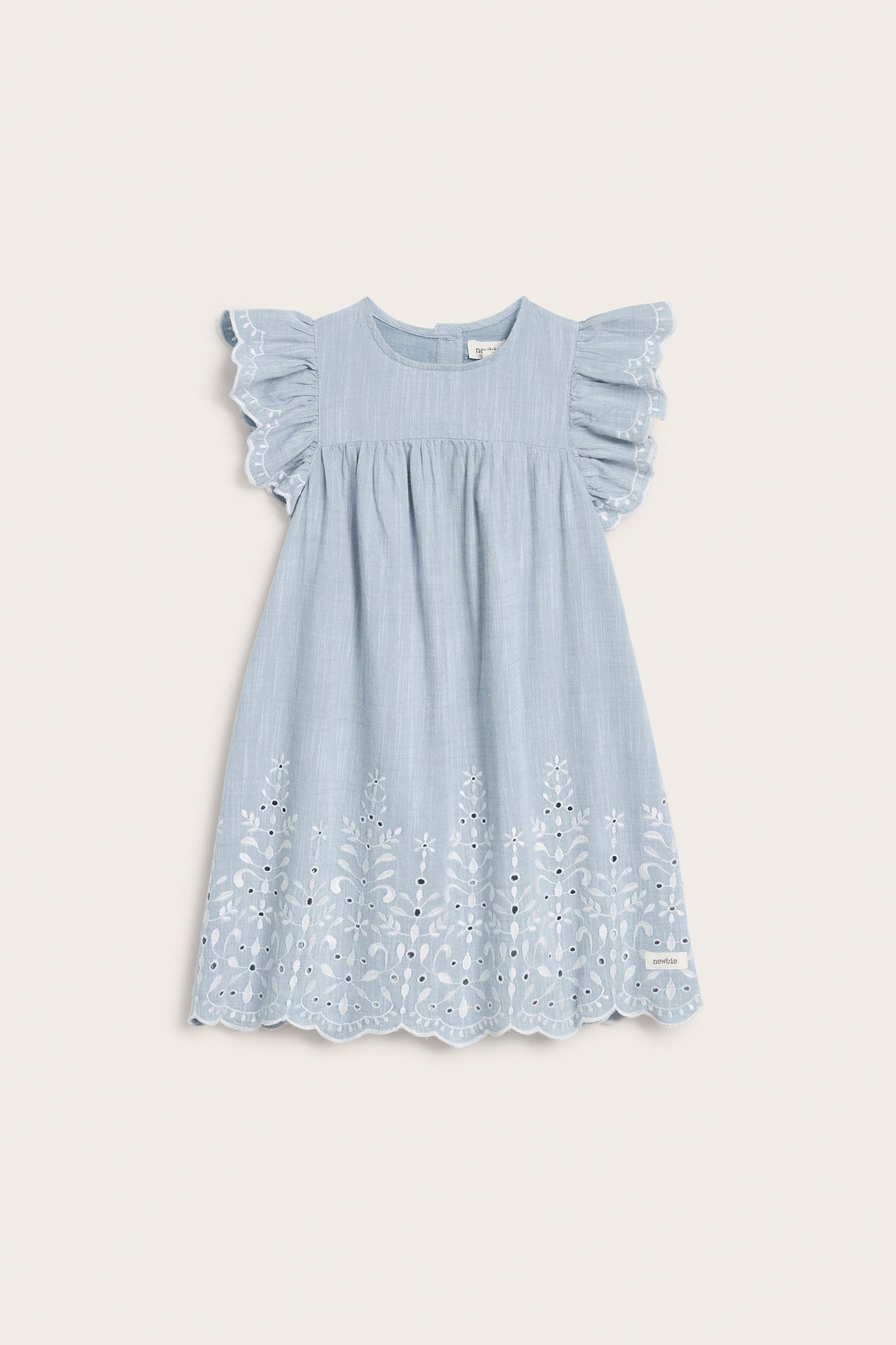 Front view of a light blue chambray kid's dress with white eyelet embroidery and ruffled cap sleeves.