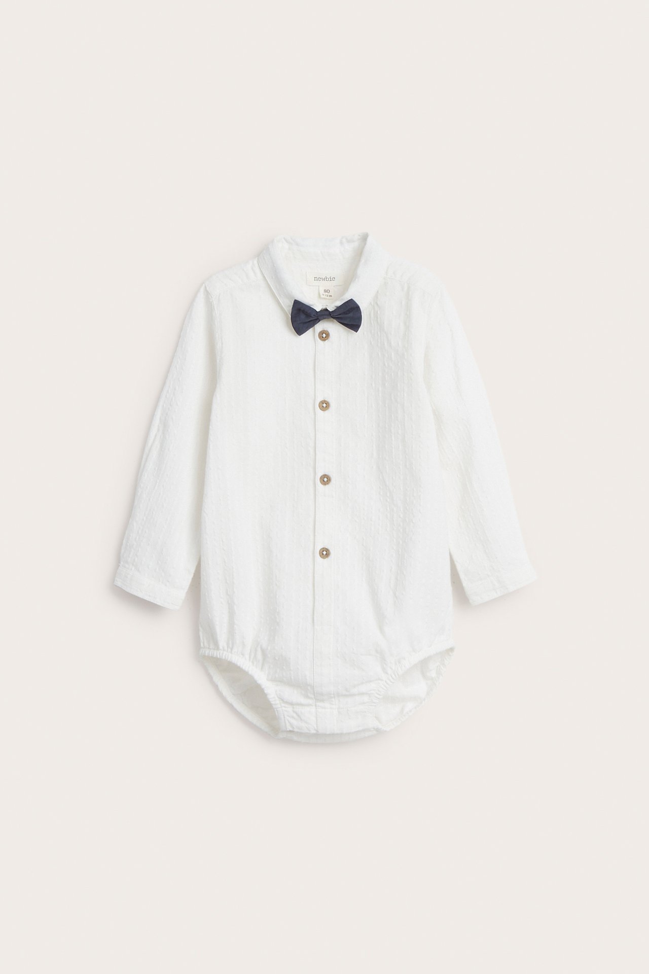 Front view of a baby's off-white woven shirt-bodysuit with a collar, long sleeves, and a dark blue bow tie.
