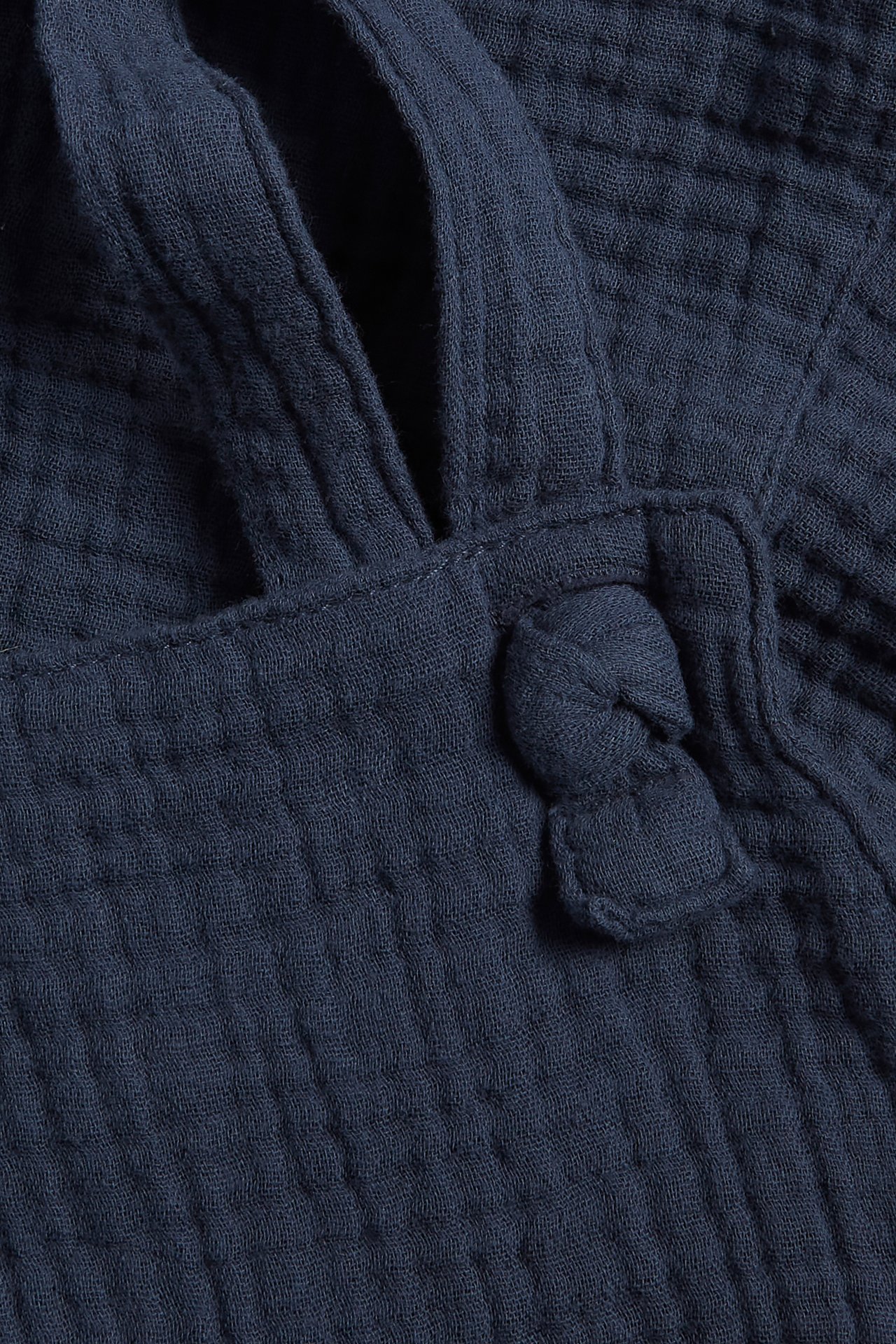 Close-up of dark blue woven cotton dungaree shorts with adjustable straps and a decorative knot.