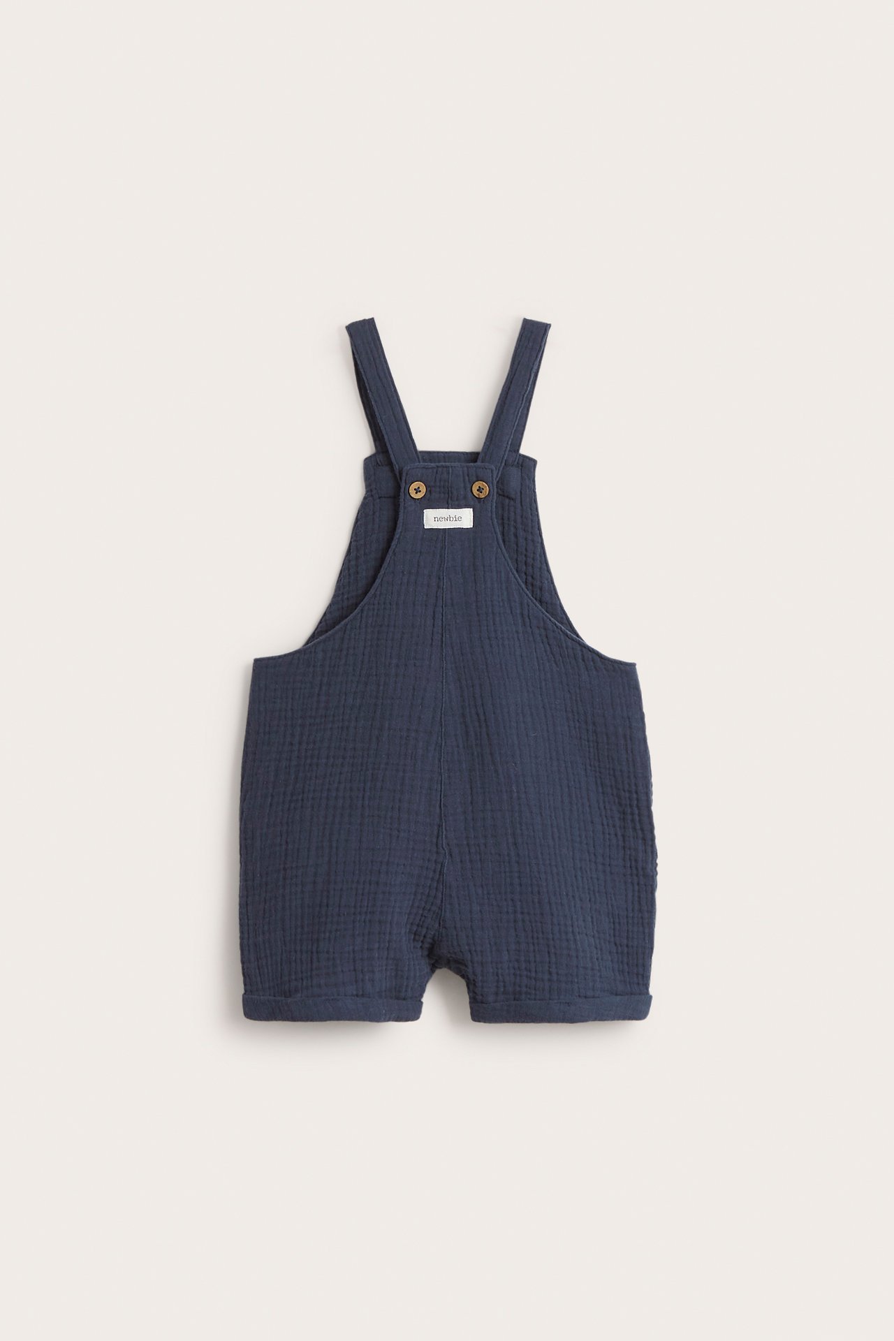 Front view of dark blue woven cotton baby's dungaree shorts with adjustable straps and wooden buttons.