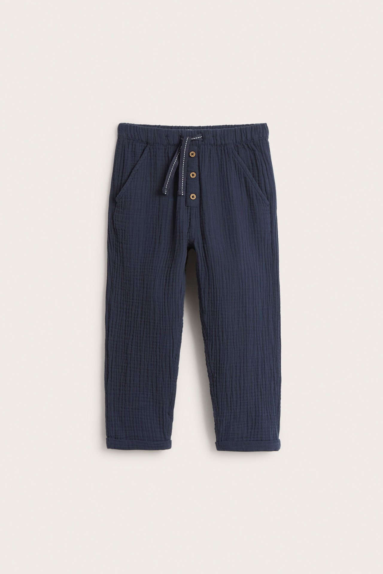 Front view of dark blue woven cotton kid's pants with elastic waist, decorative buttons, and rolled-up cuffs.