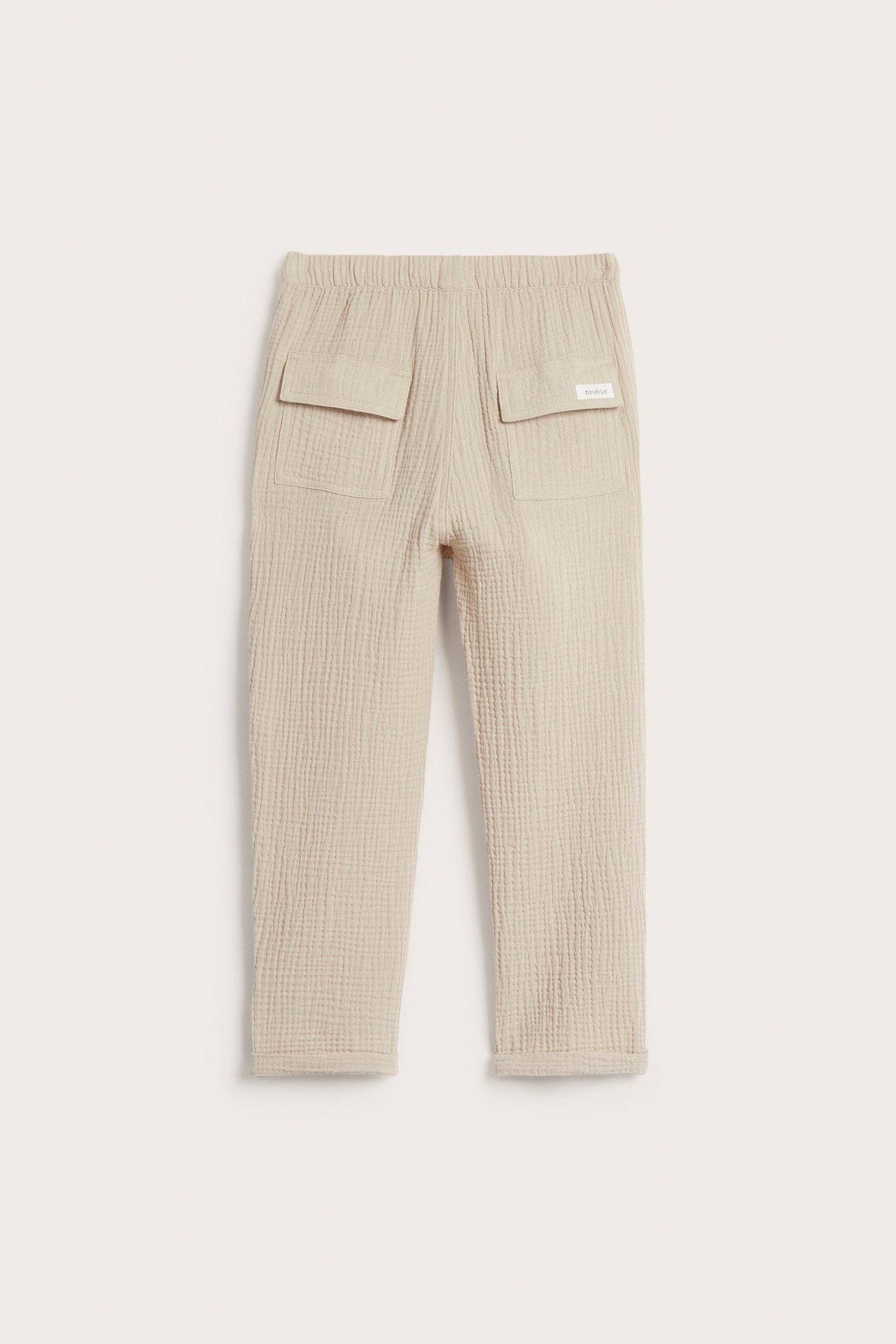 Back view of beige woven cotton pants with elastic waist, back flap pockets, and rolled cuffs.