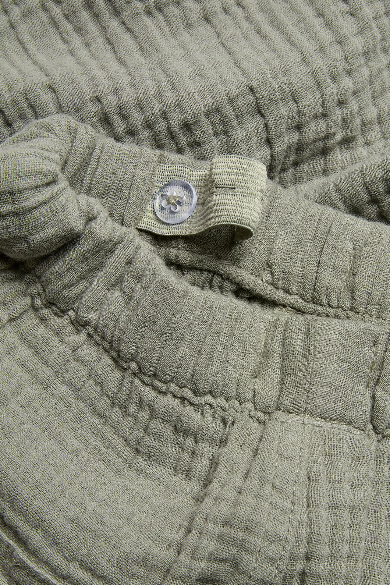 Close-up of green woven cotton pants with an adjustable elastic waist and clear button.