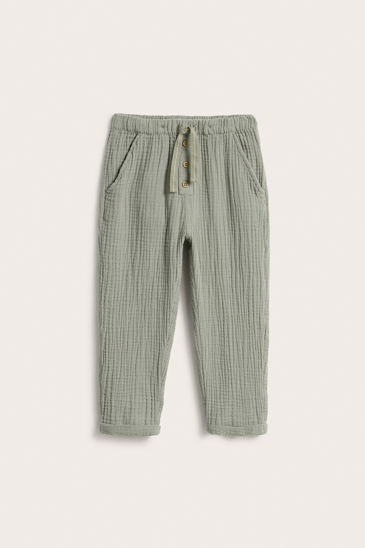 Front view of green woven cotton pants with elastic waist, decorative drawstring, and rolled-up cuffs.