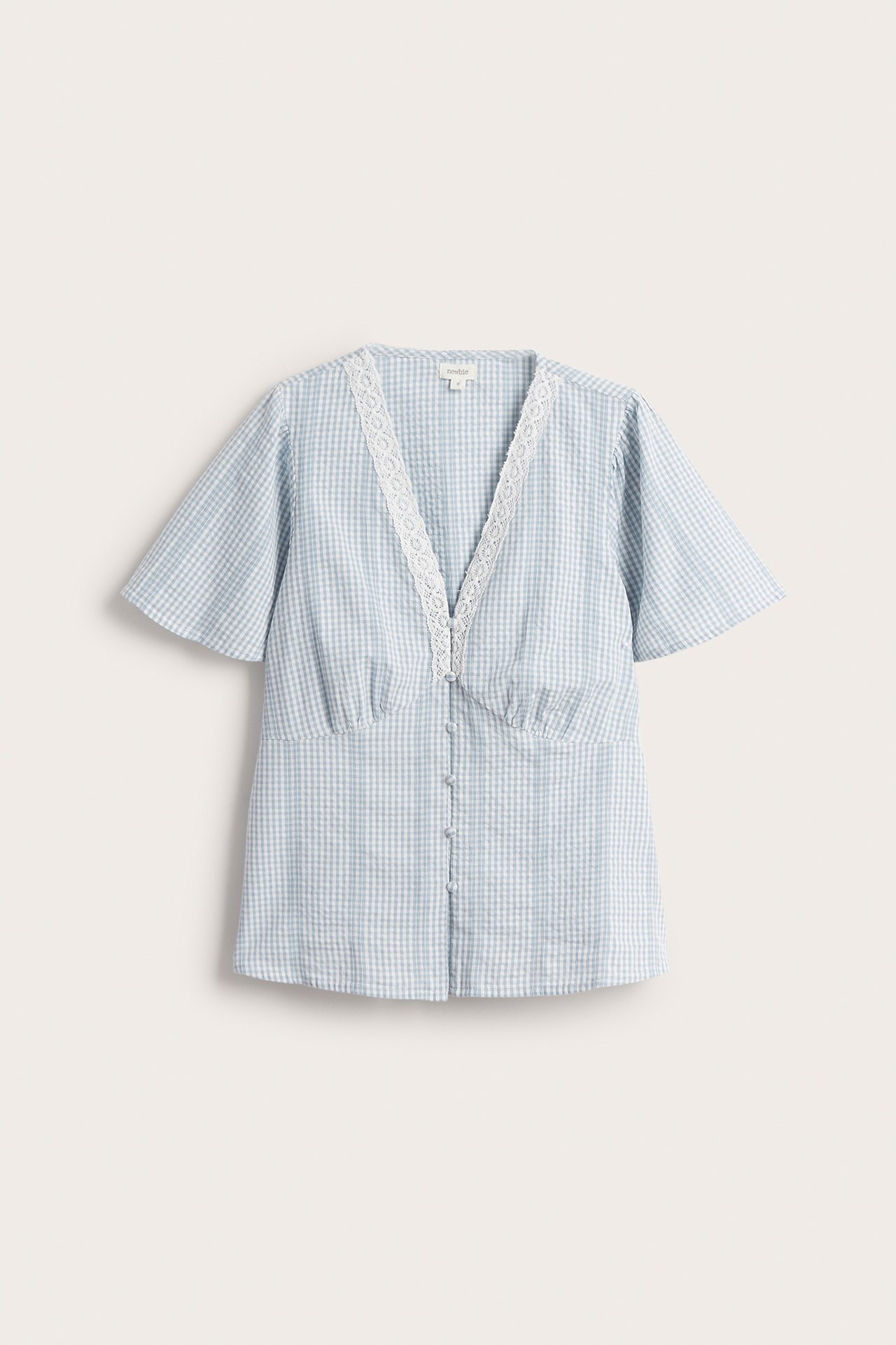 Front view of a woman's light blue and off-white checked cotton blouse with a lace-trimmed V-neck and short flared sleeves.